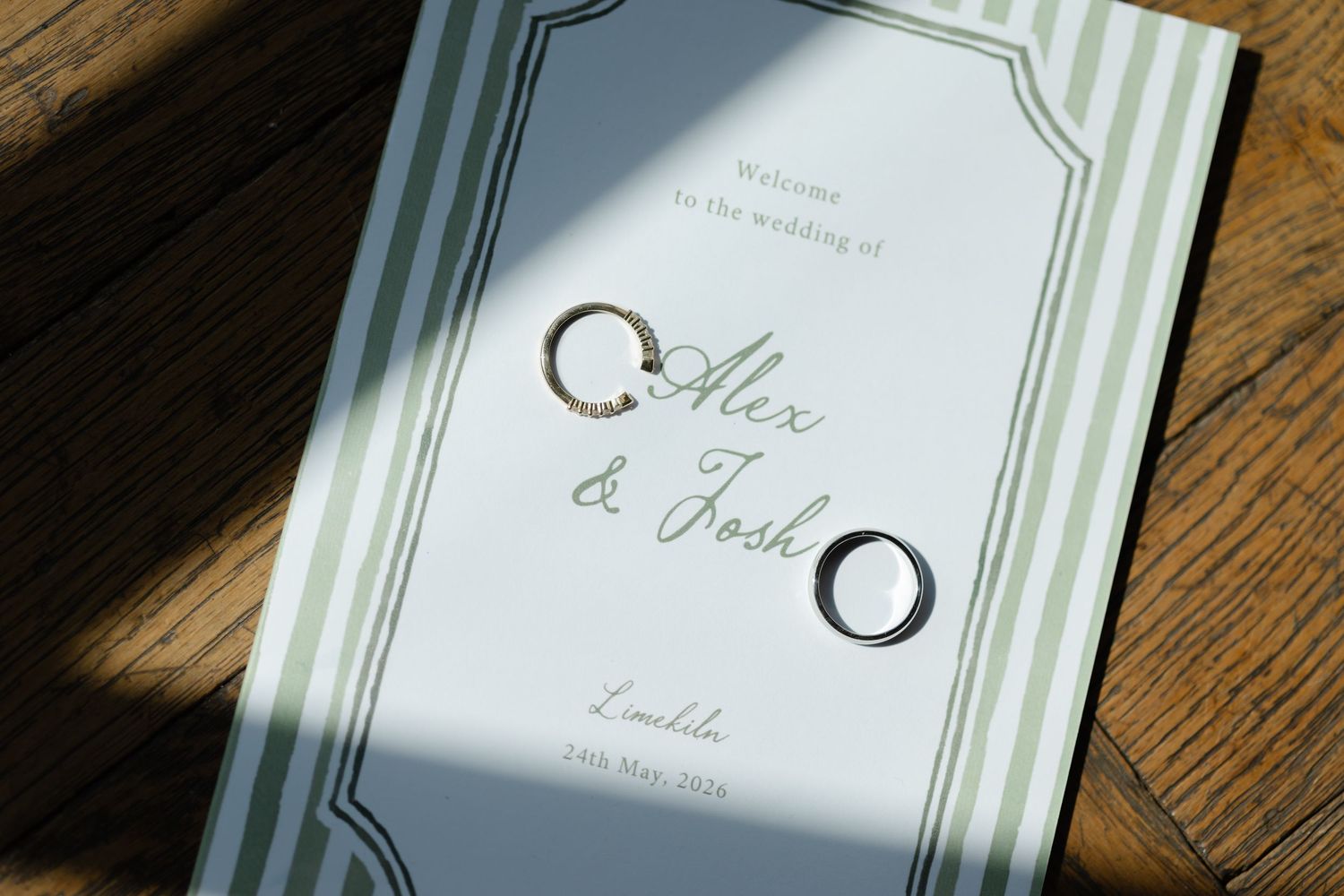 Wedding program booklet for Alex and Josh with two gold rings resting on a green striped cover.