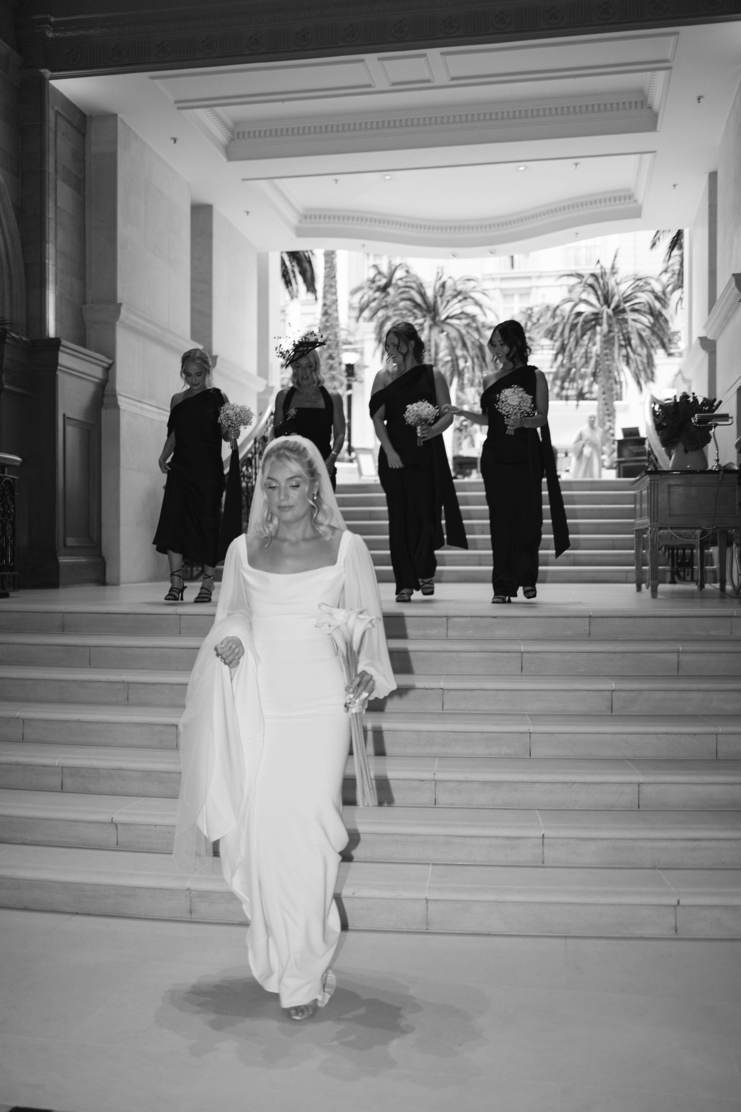 Wedding party descending grand white marble staircase in formal attire.