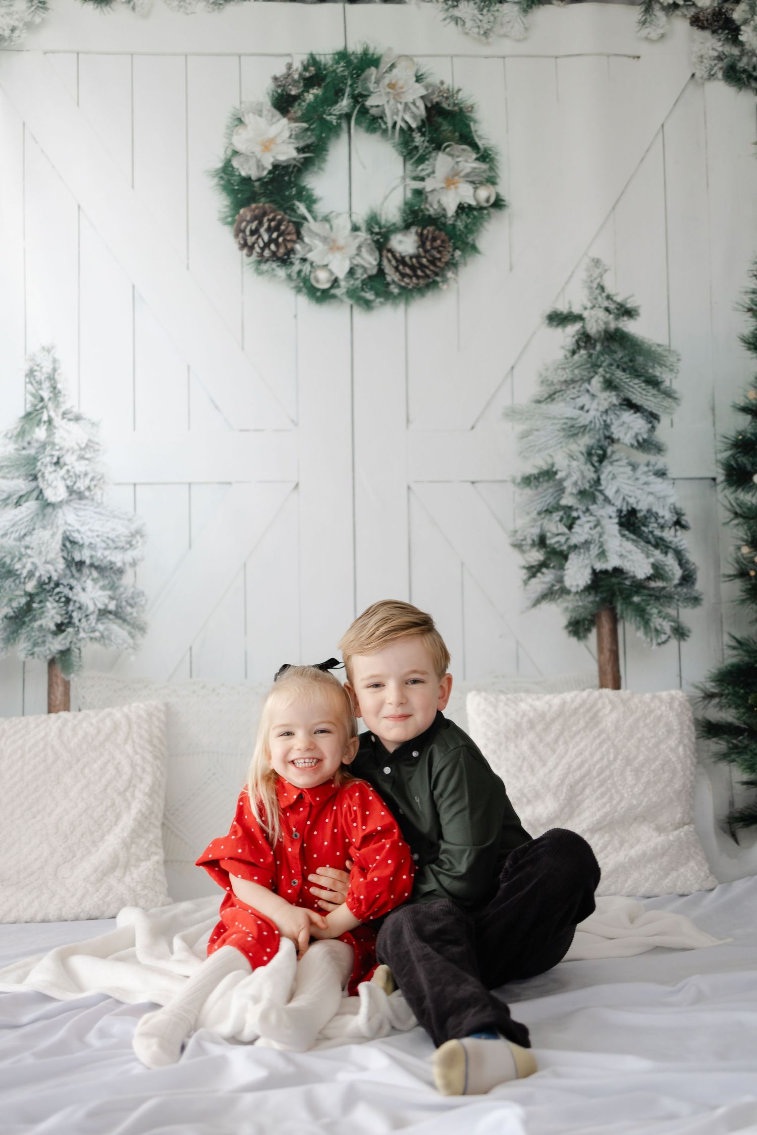 Children in holiday outfits sitting together in a winter wonderland photo setting.