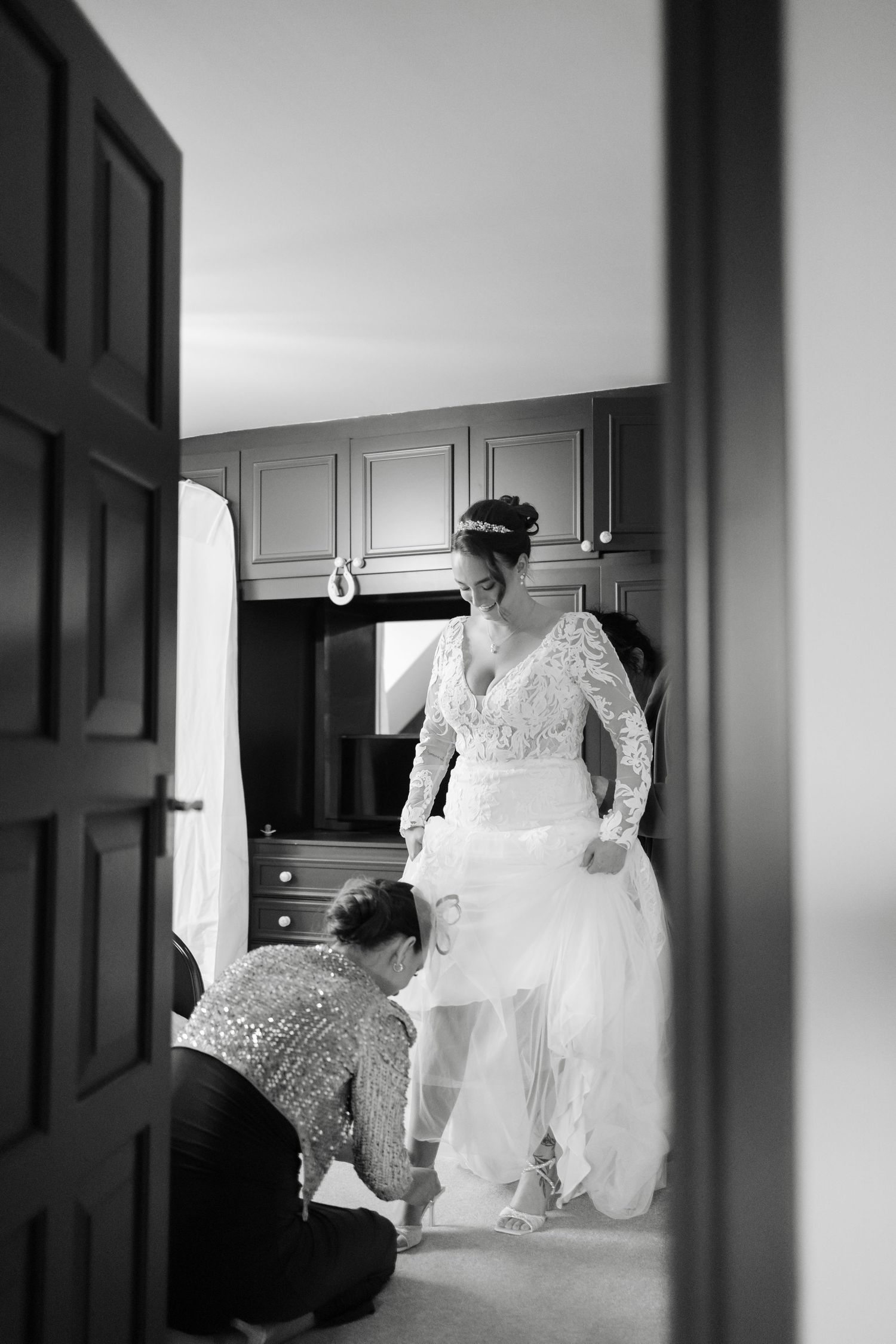 Black and white photo of wedding dress preparations through doorway.