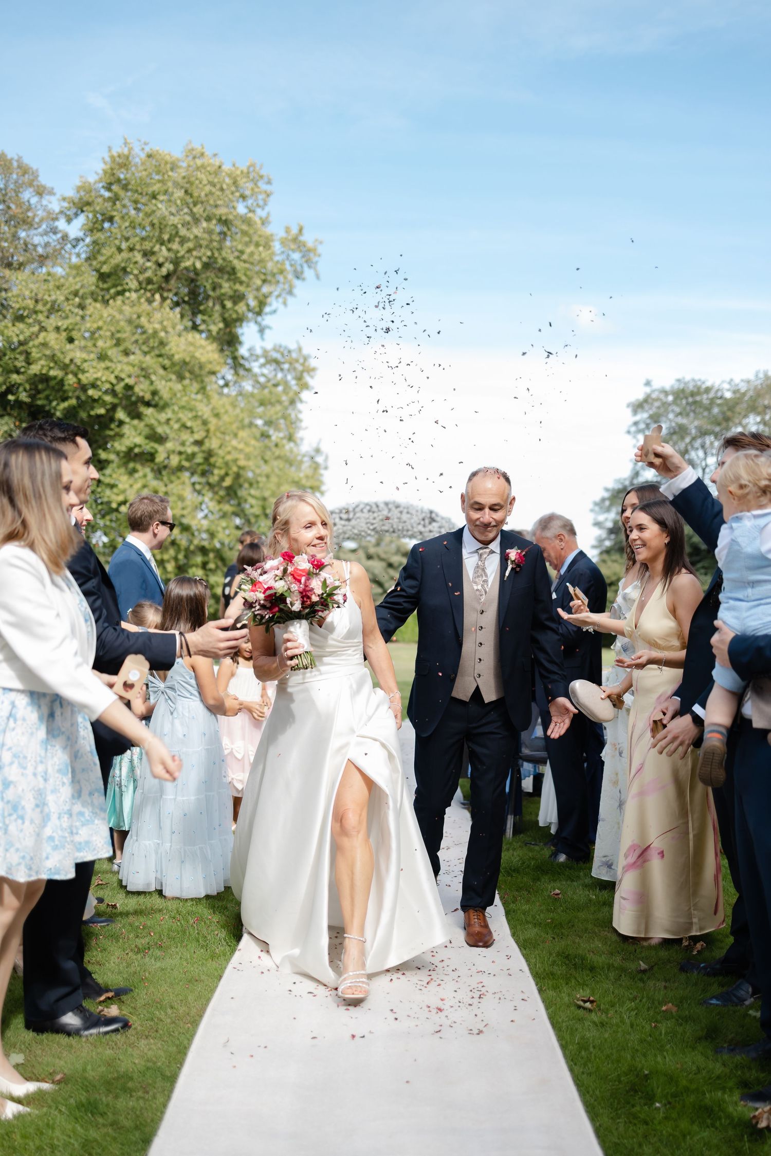Wedding guests celebrate by throwing confetti during an outdoor garden reception.