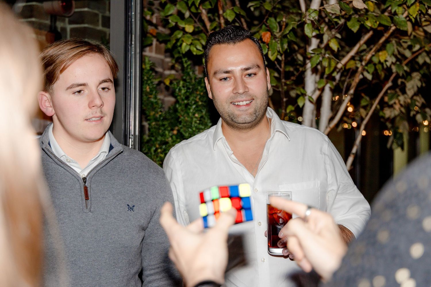 People gathered around watching someone solve a colorful Rubik's cube puzzle.