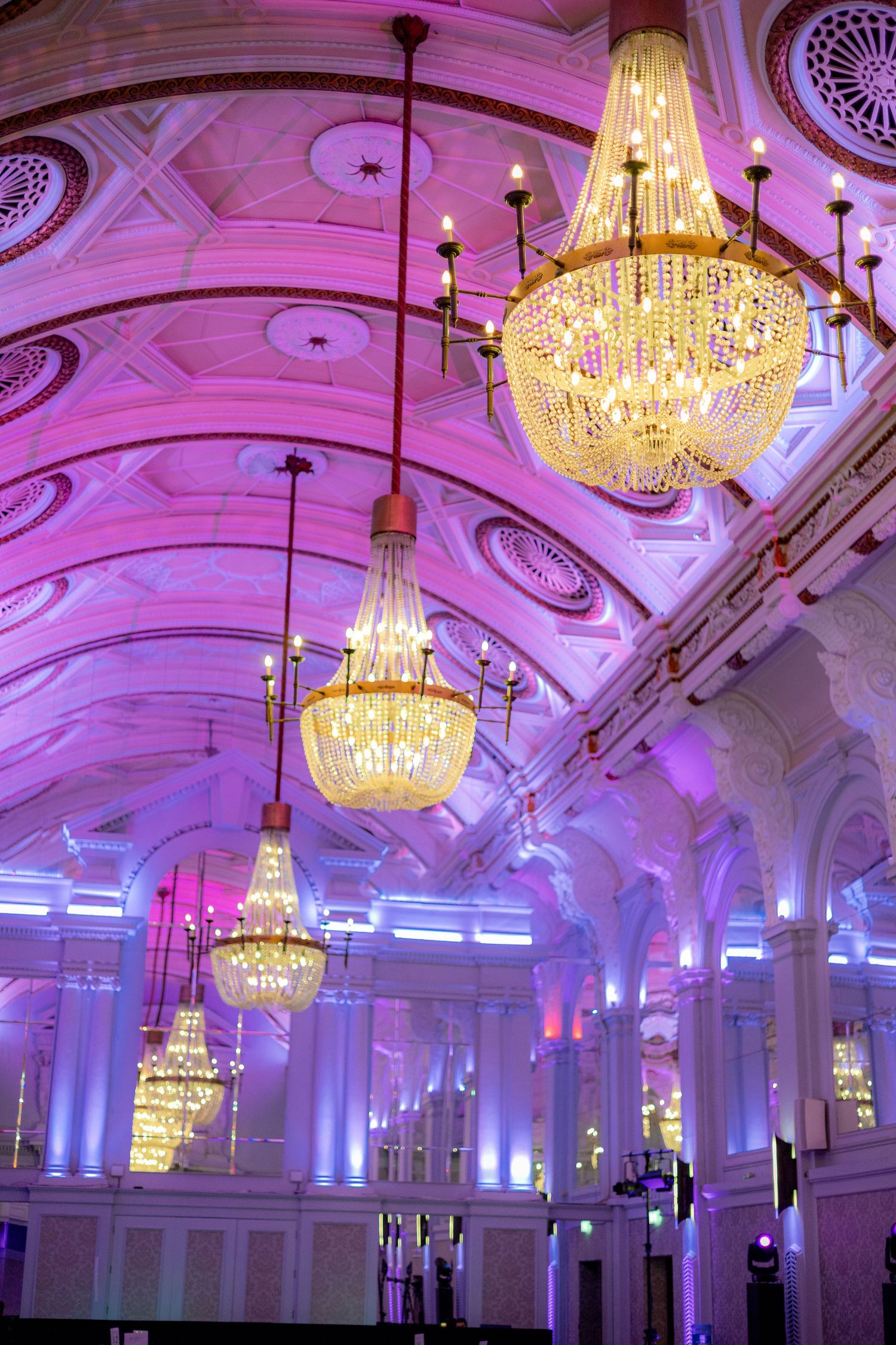Grand ballroom with ornate chandeliers and purple uplighting creating dramatic atmosphere.