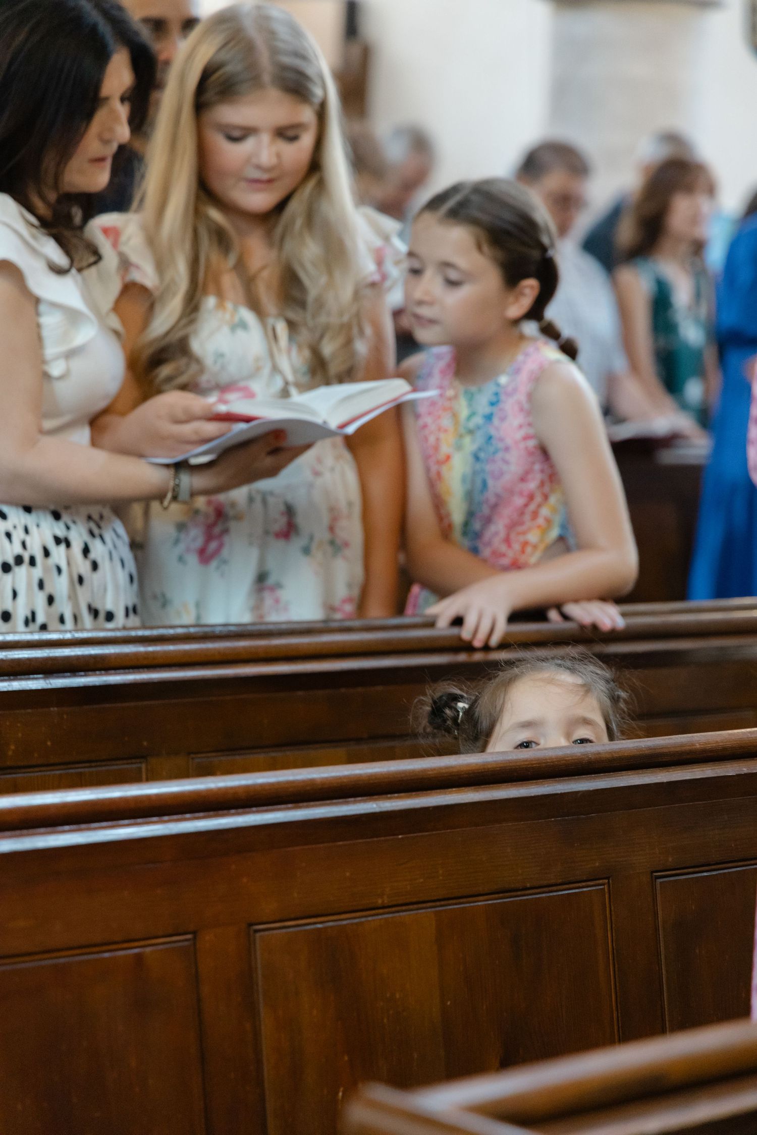Young attendees peek over wooden church pews during a ceremony.