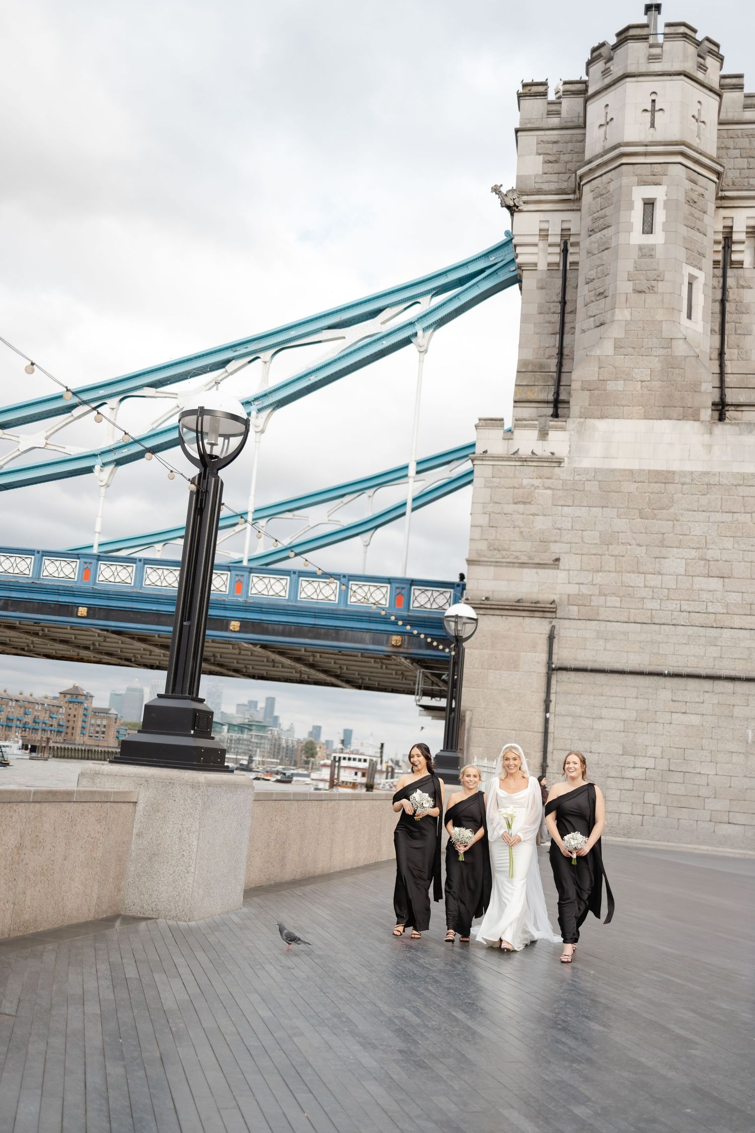 Wedding party walking along Tower Bridge with bridesmaids in black dresses.