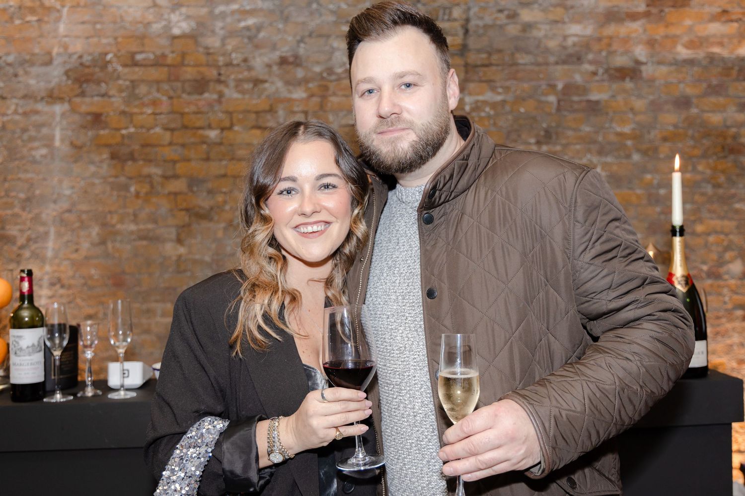Guests sharing drinks and smiles at brick-walled venue.