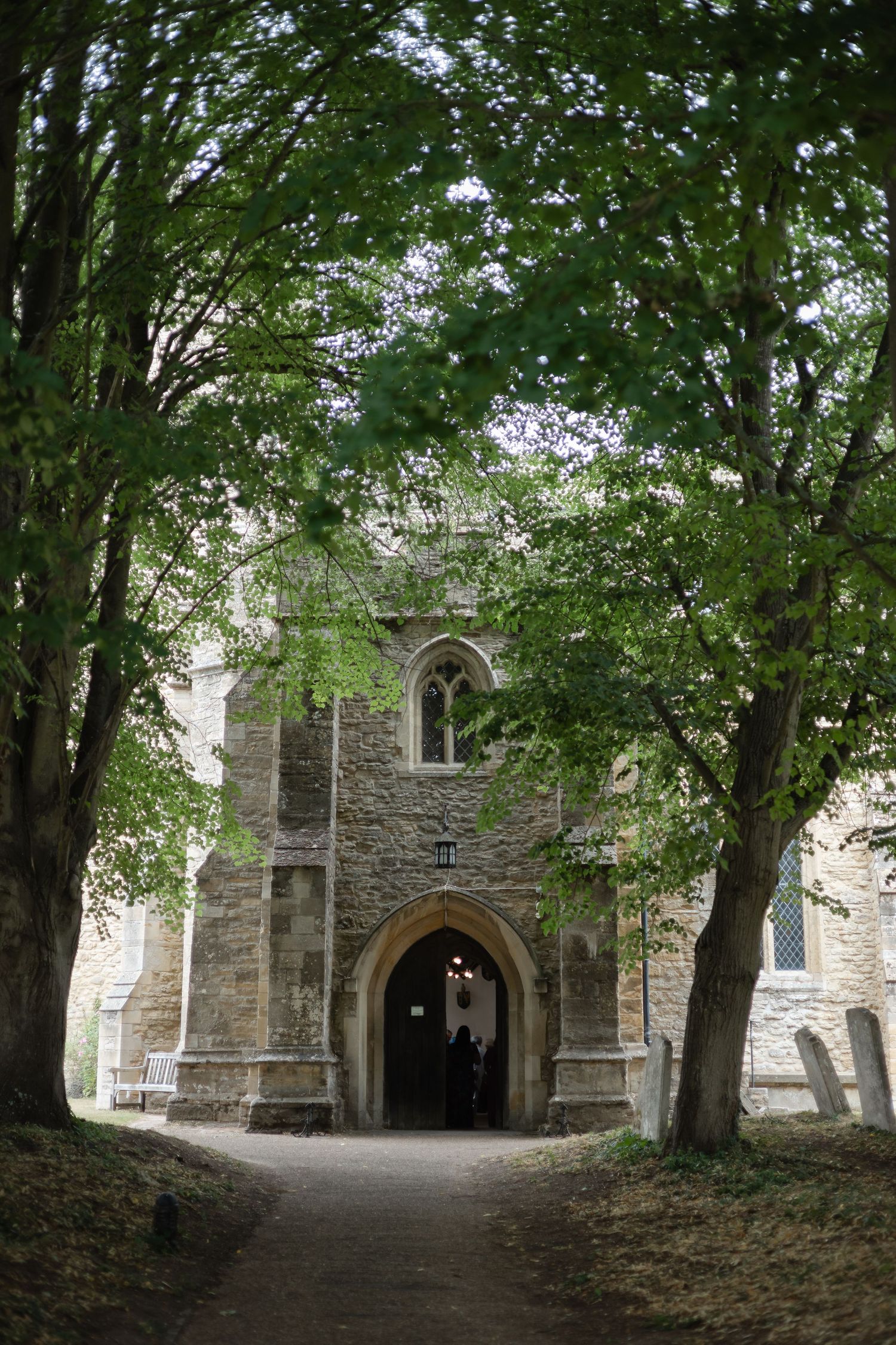Stone church exterior with Gothic archway surrounded by green trees.