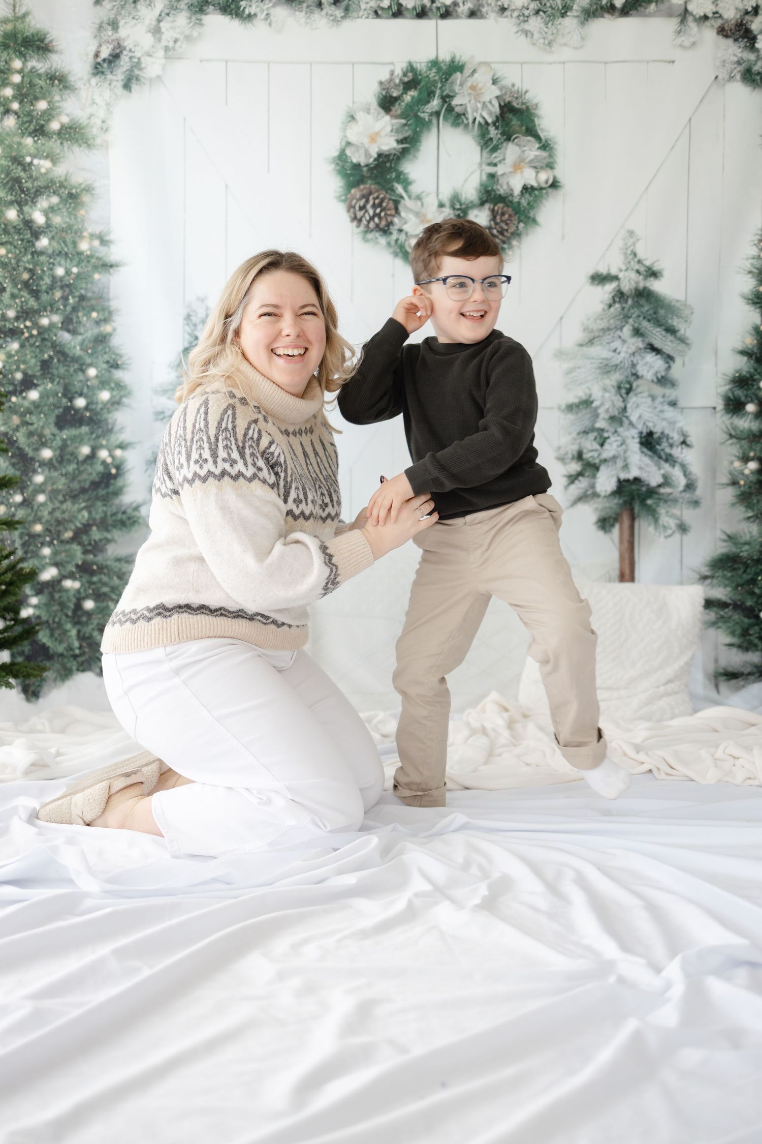Playful winter holiday photo with festive backdrop of snowy trees and wreath.