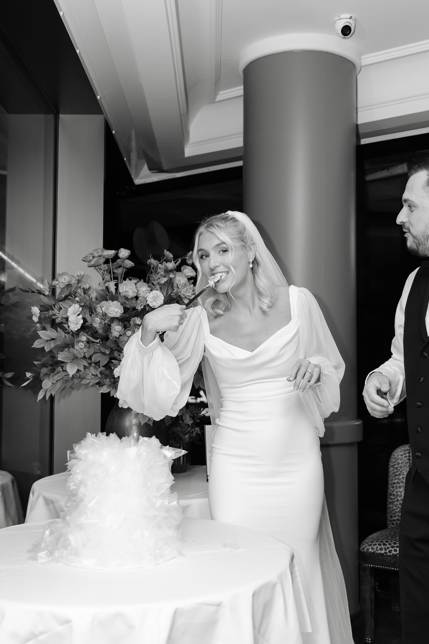 Elegant white wedding dress displayed with floral arrangements in an indoor venue.