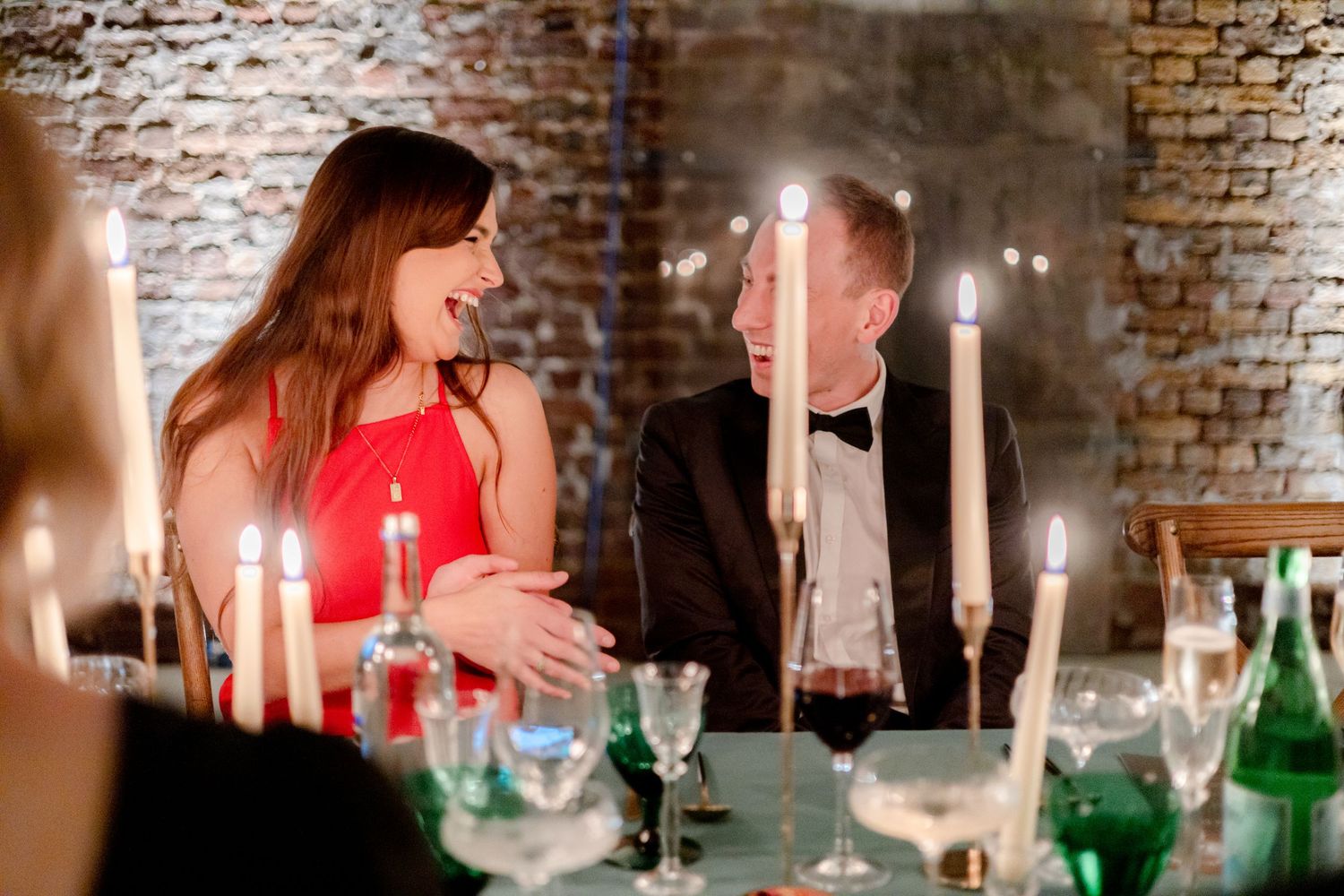 Elegant dinner party setting with candles and wine glasses against exposed brick walls.
