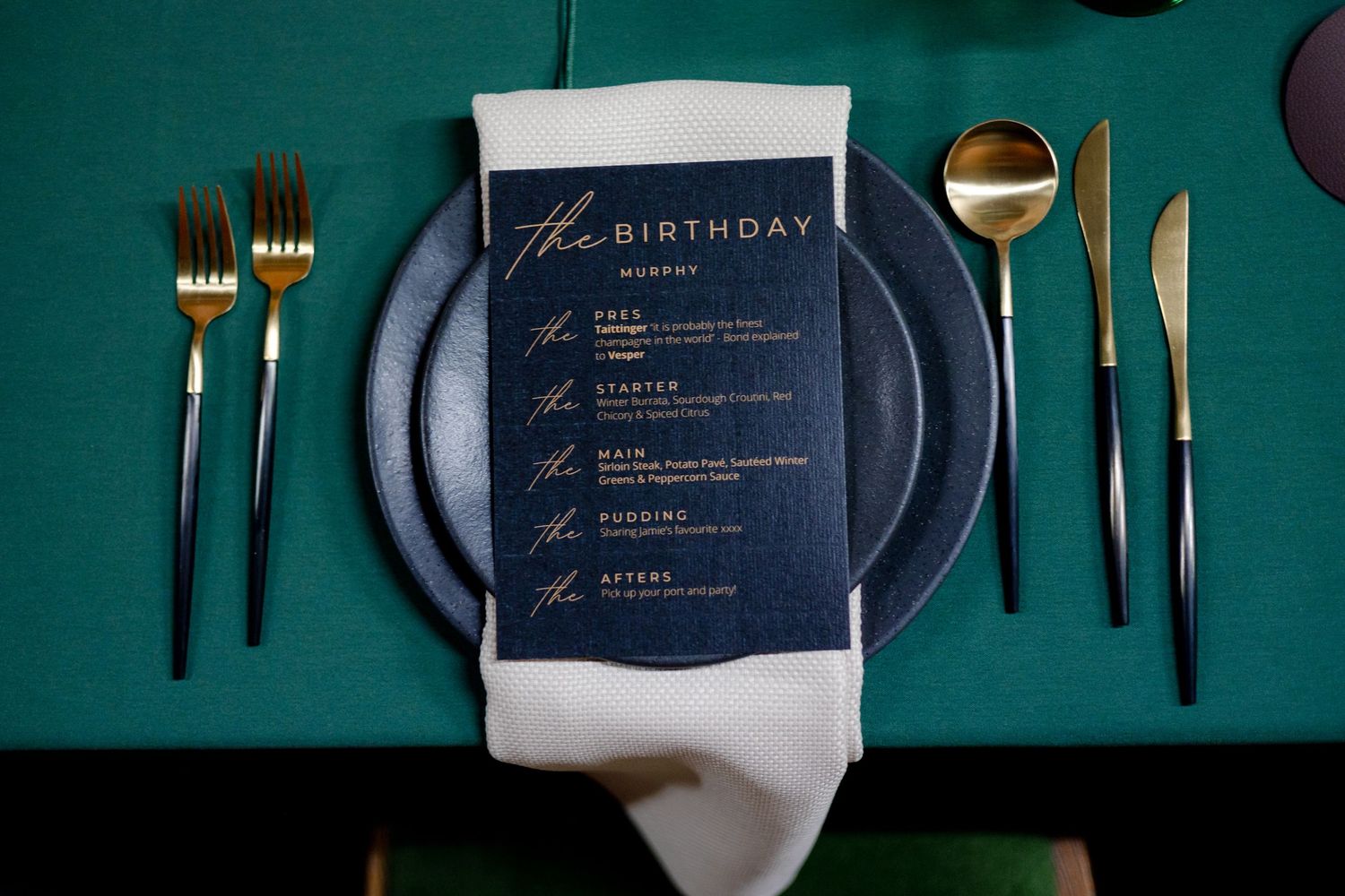 Elegant place settings with navy blue menus and gold cutlery on emerald green tablecloths.