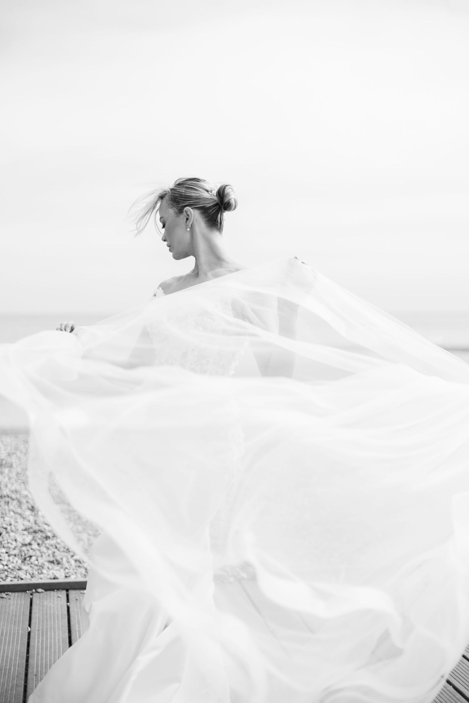 Flowing white wedding dress veil blowing dramatically in the wind against light background.