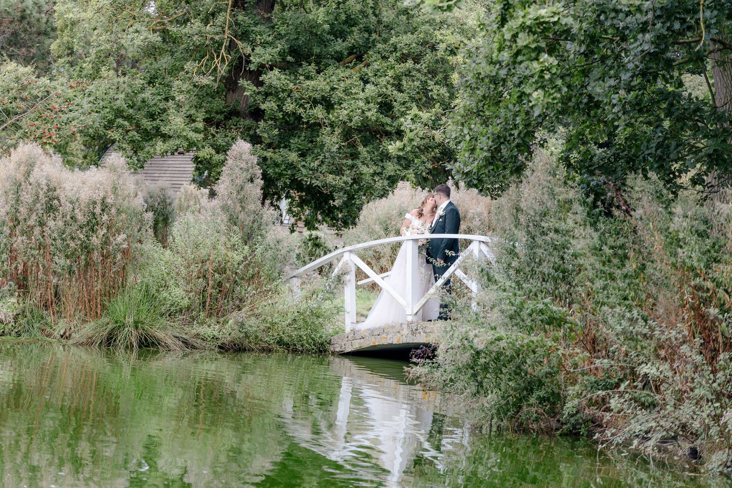 Scenic wedding photography near a pond with white bridge and natural surroundings.