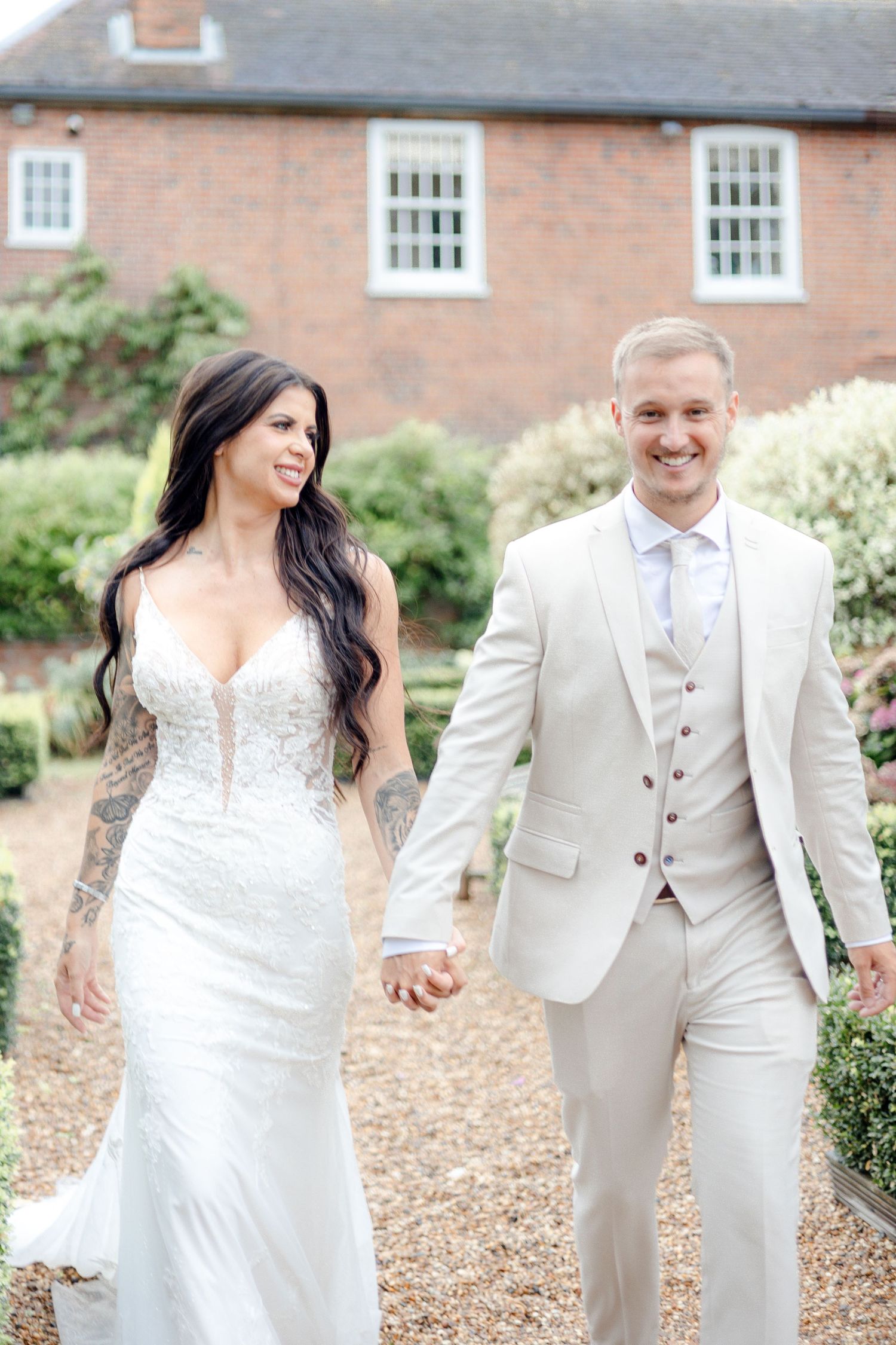 A wedding couple shares a romantic moment on a brick pathway outside a historic building.