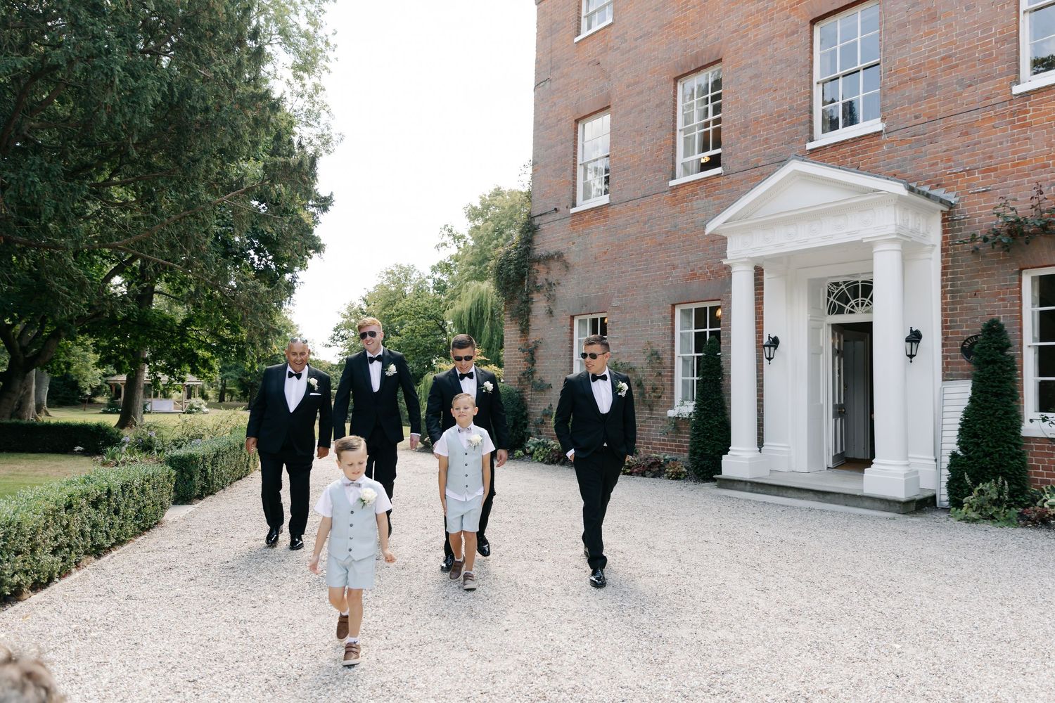 Wedding party walking along a brick building exterior pathway.