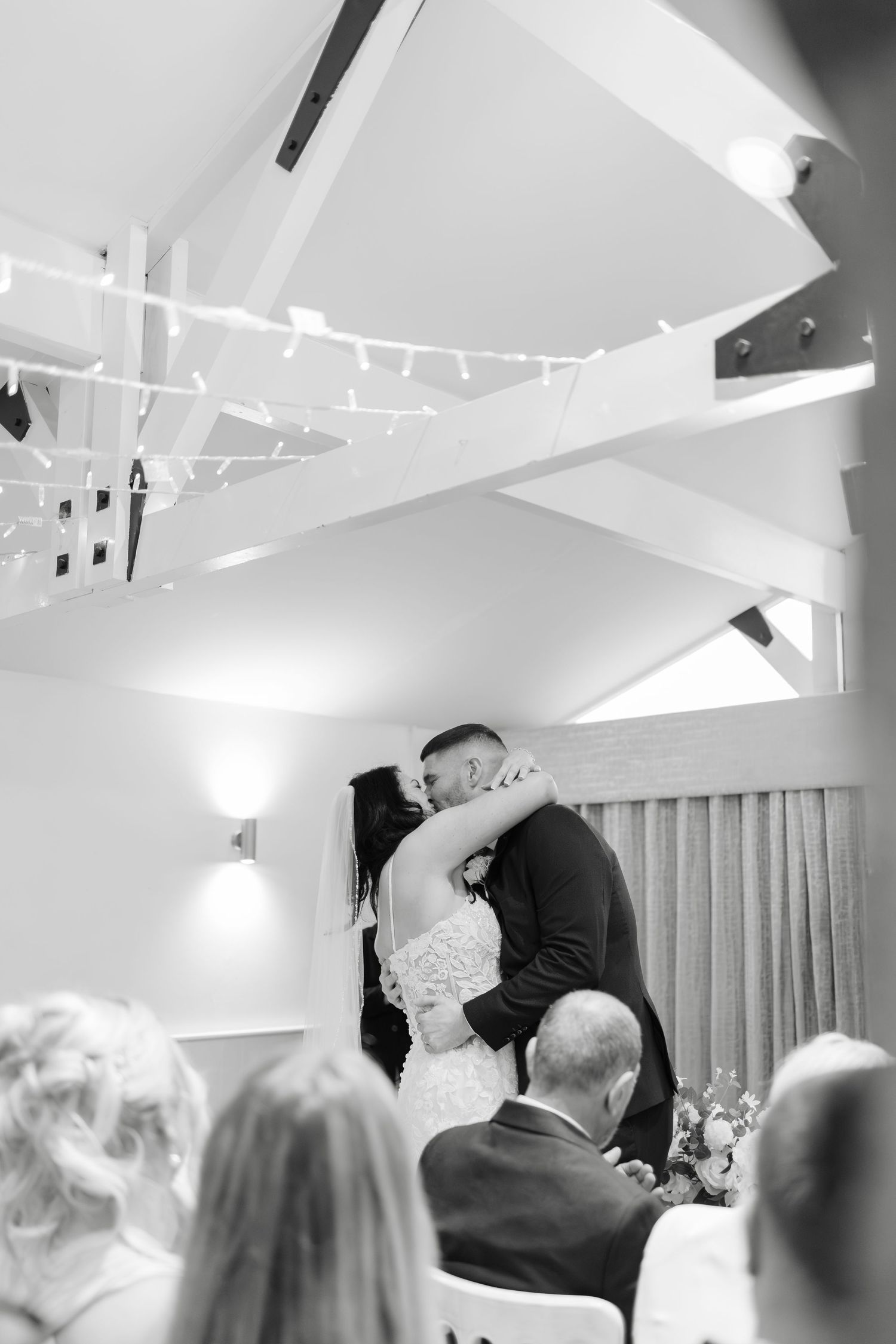 Wedding reception scene in bright white room with vaulted ceilings and hanging lights.