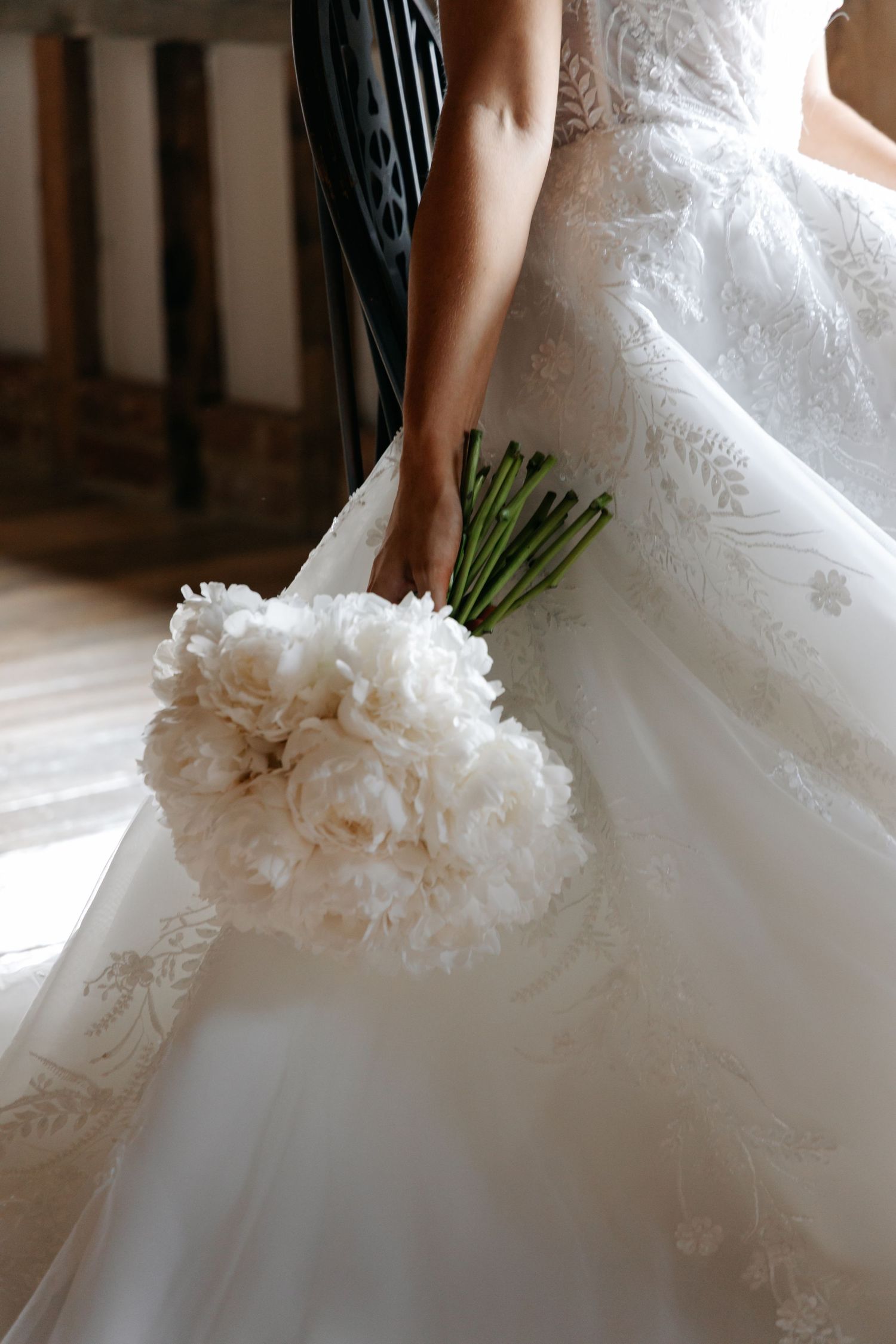 Close-up of white wedding dress details and bouquet against wooden floor.