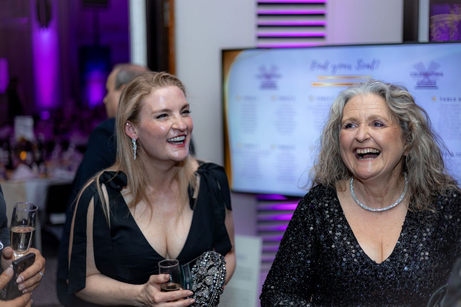 Women in evening wear sharing laughs at an elegant awards ceremony.