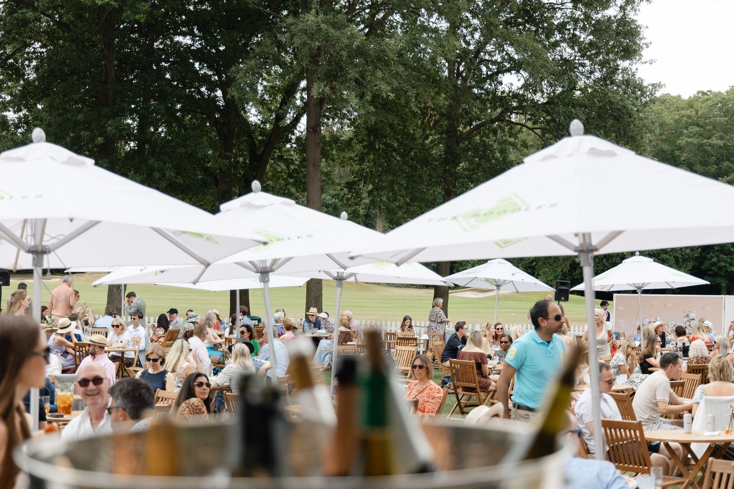 Outdoor event setup with white tents and tables arranged on a sunny lawn.