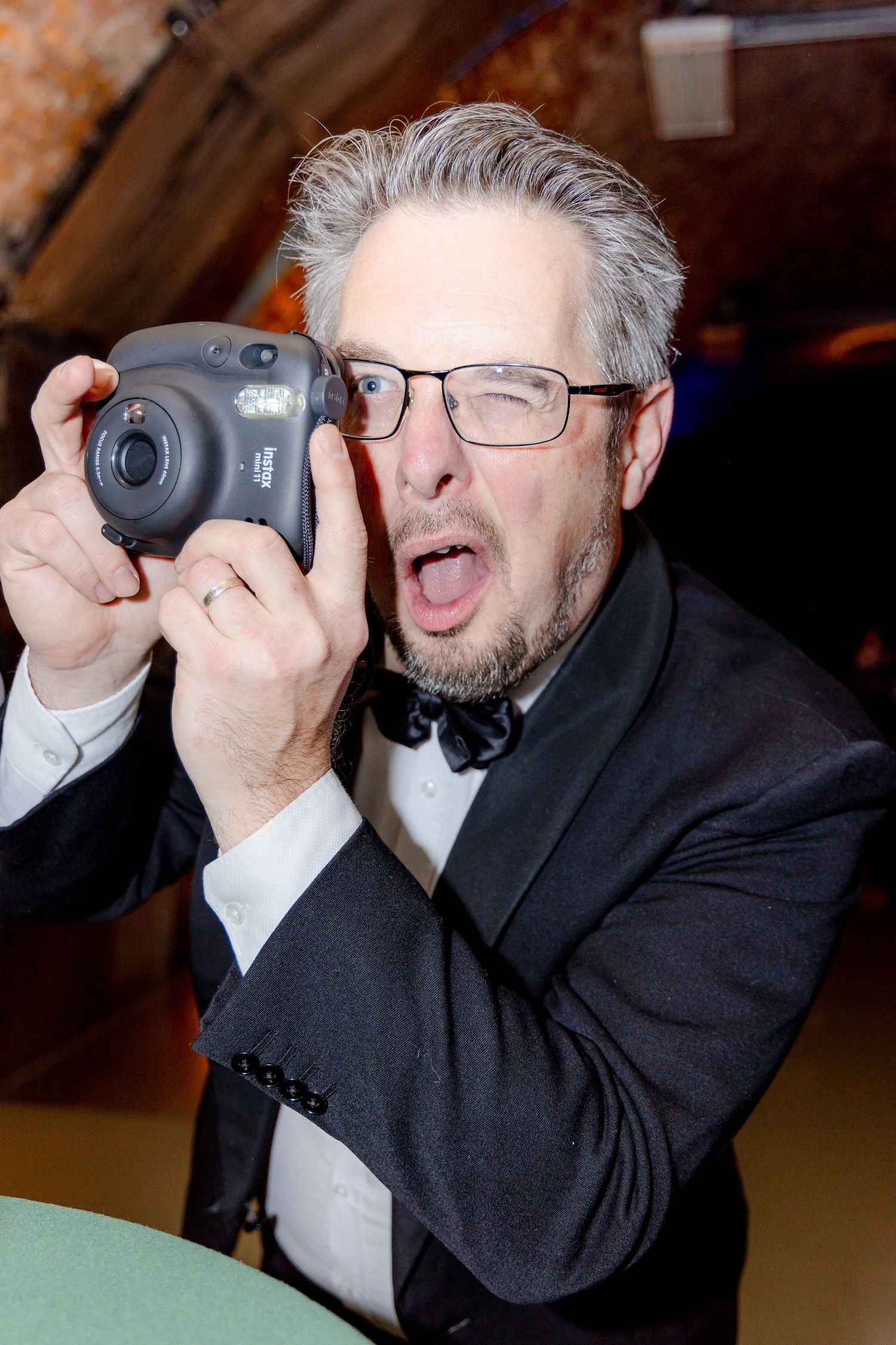 Photographer in formal attire enthusiastically taking pictures with an instant camera.