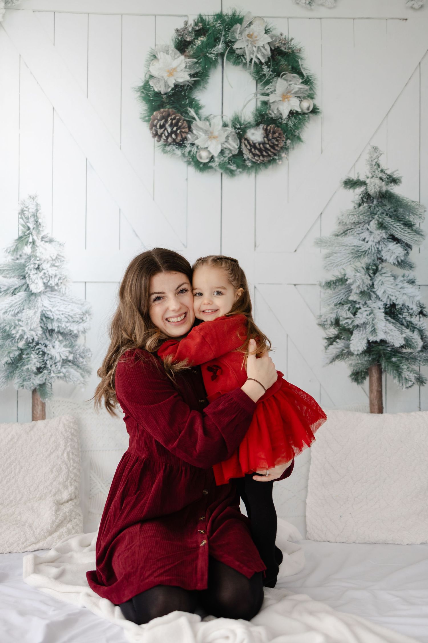 A cozy winter portrait scene with a decorated wreath and snowy trees in the background.
