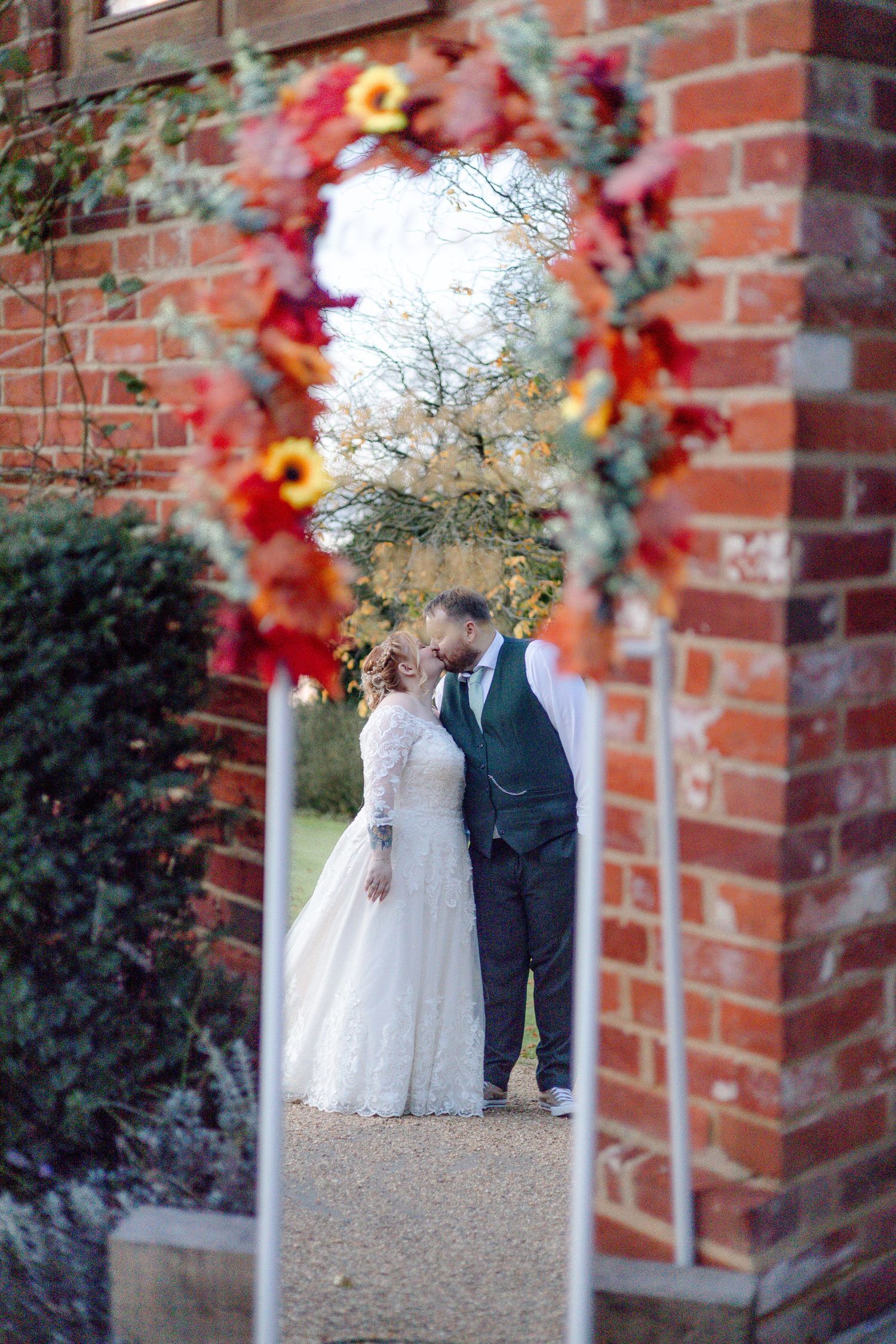 A romantic wedding photo sequence through a brick archway with autumn foliage decorations.