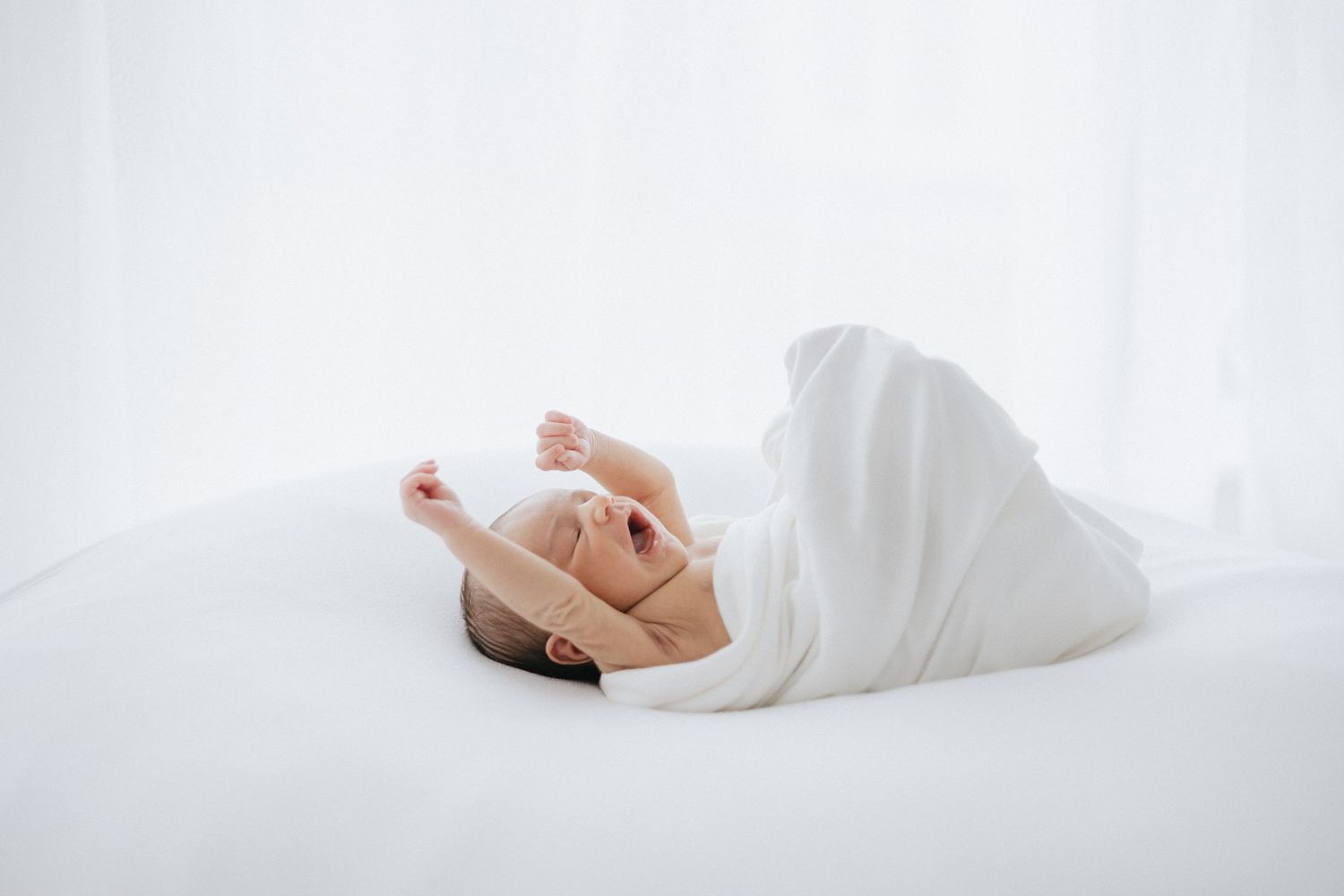 Minimalist high-key portrait of a sleeping figure wrapped in white bedding.