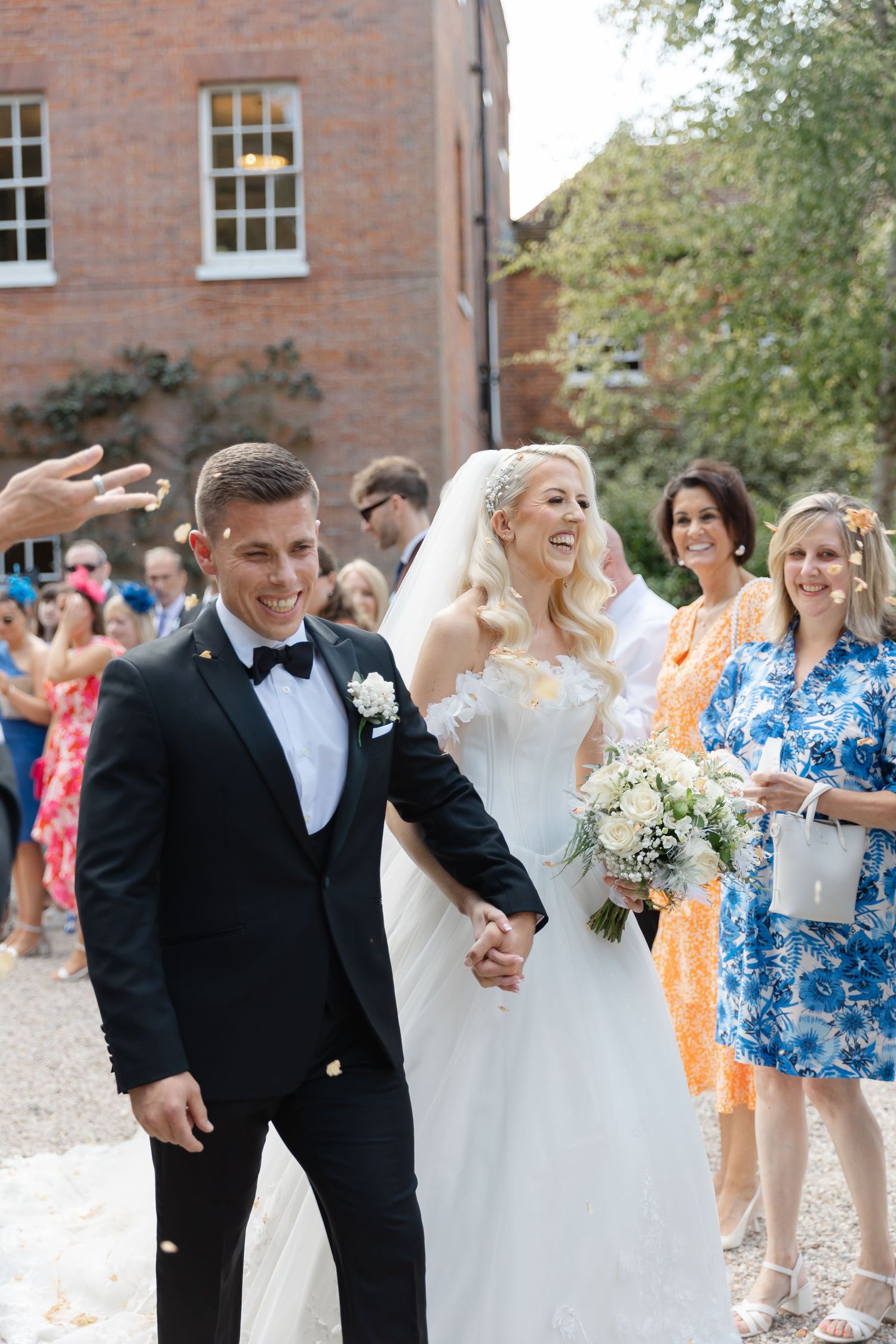 Wedding celebration outside historic brick building with guests throwing confetti.