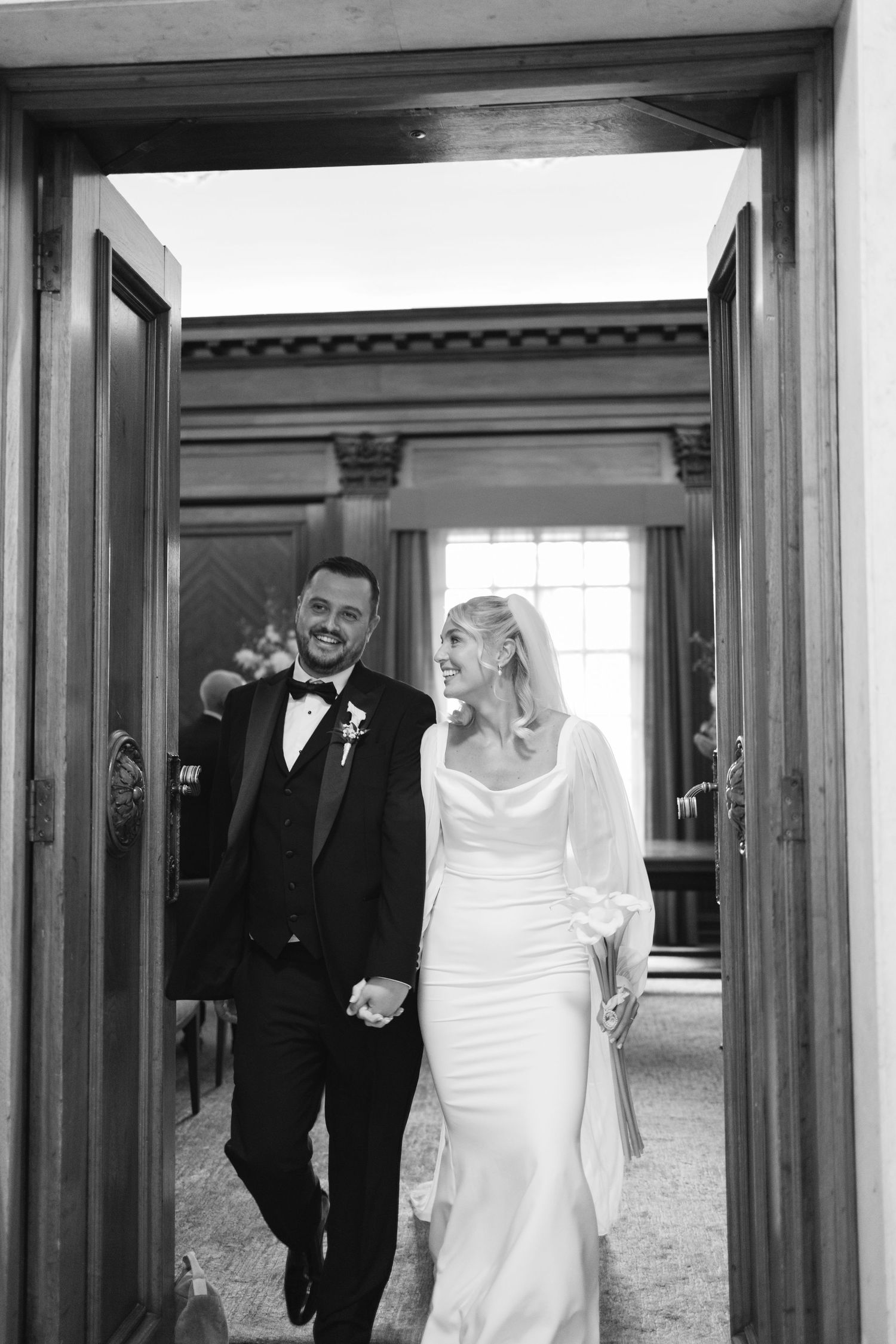 Wedding couple walking through elegant wooden doorways in formal attire.