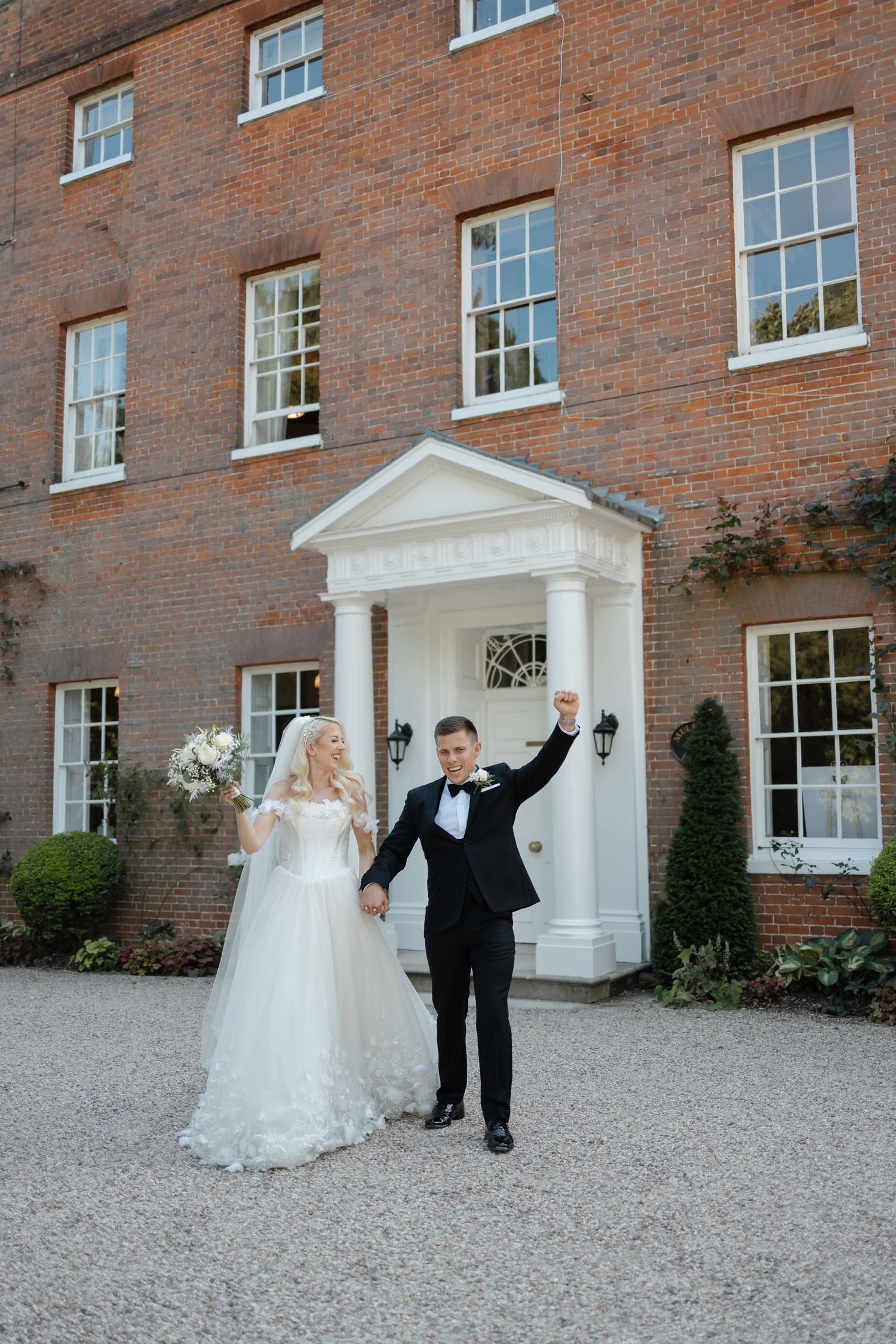 Wedding couple celebrates outside historic brick mansion with white columned entrance.