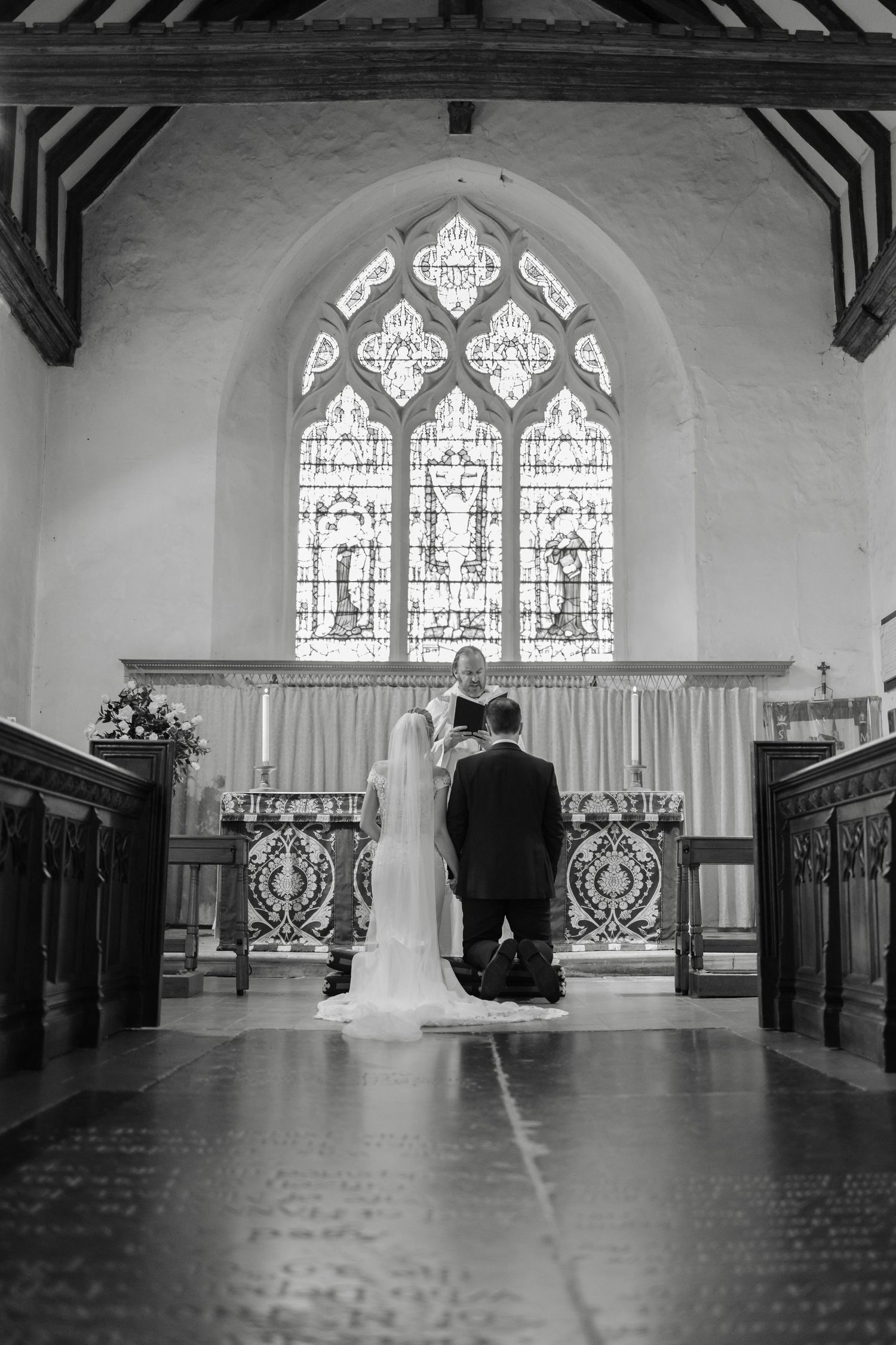 Church interior with stained glass windows and wooden beams in black and white.