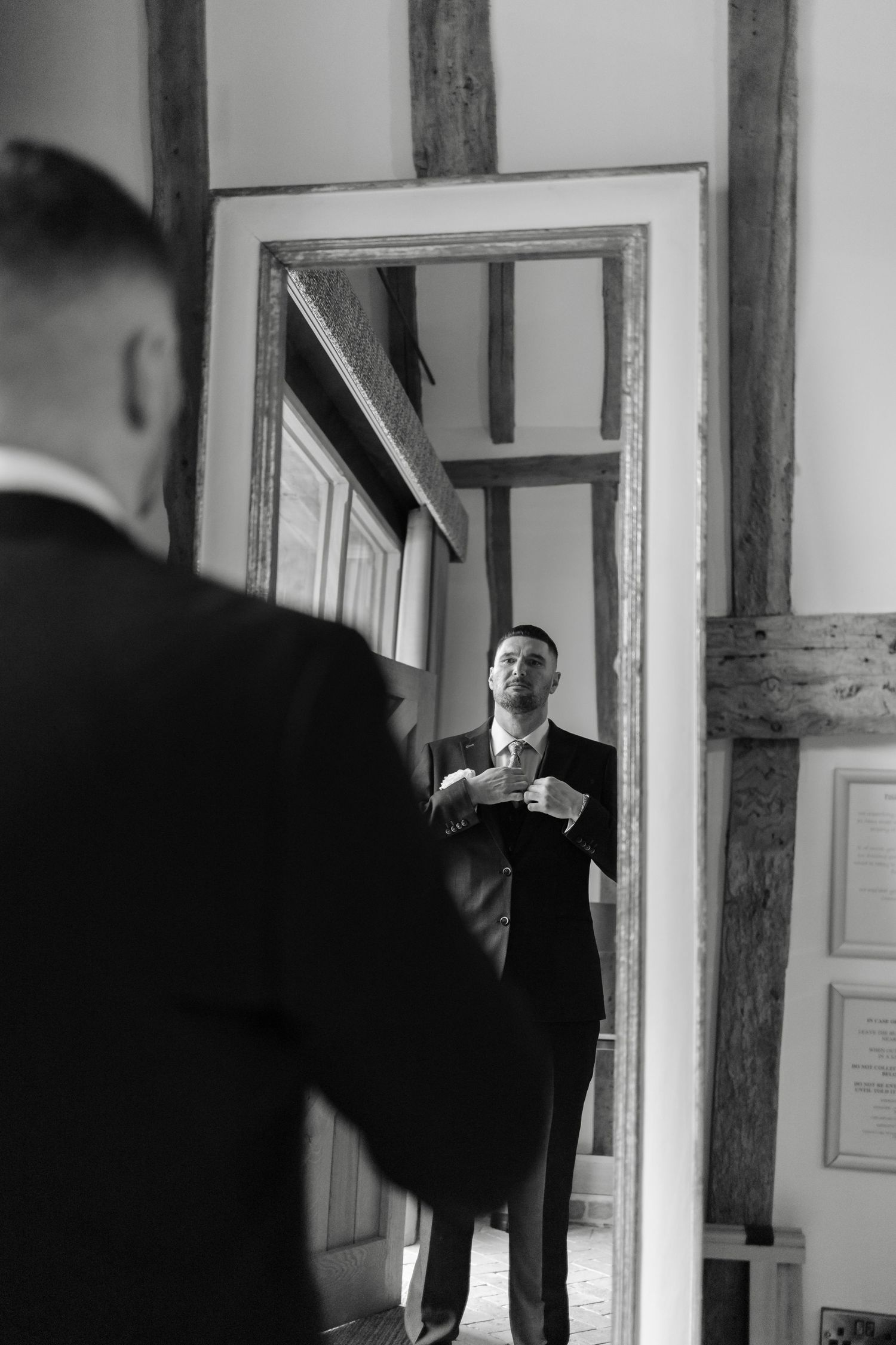 Black and white photo of groom getting ready in vintage hallway with mirrors.