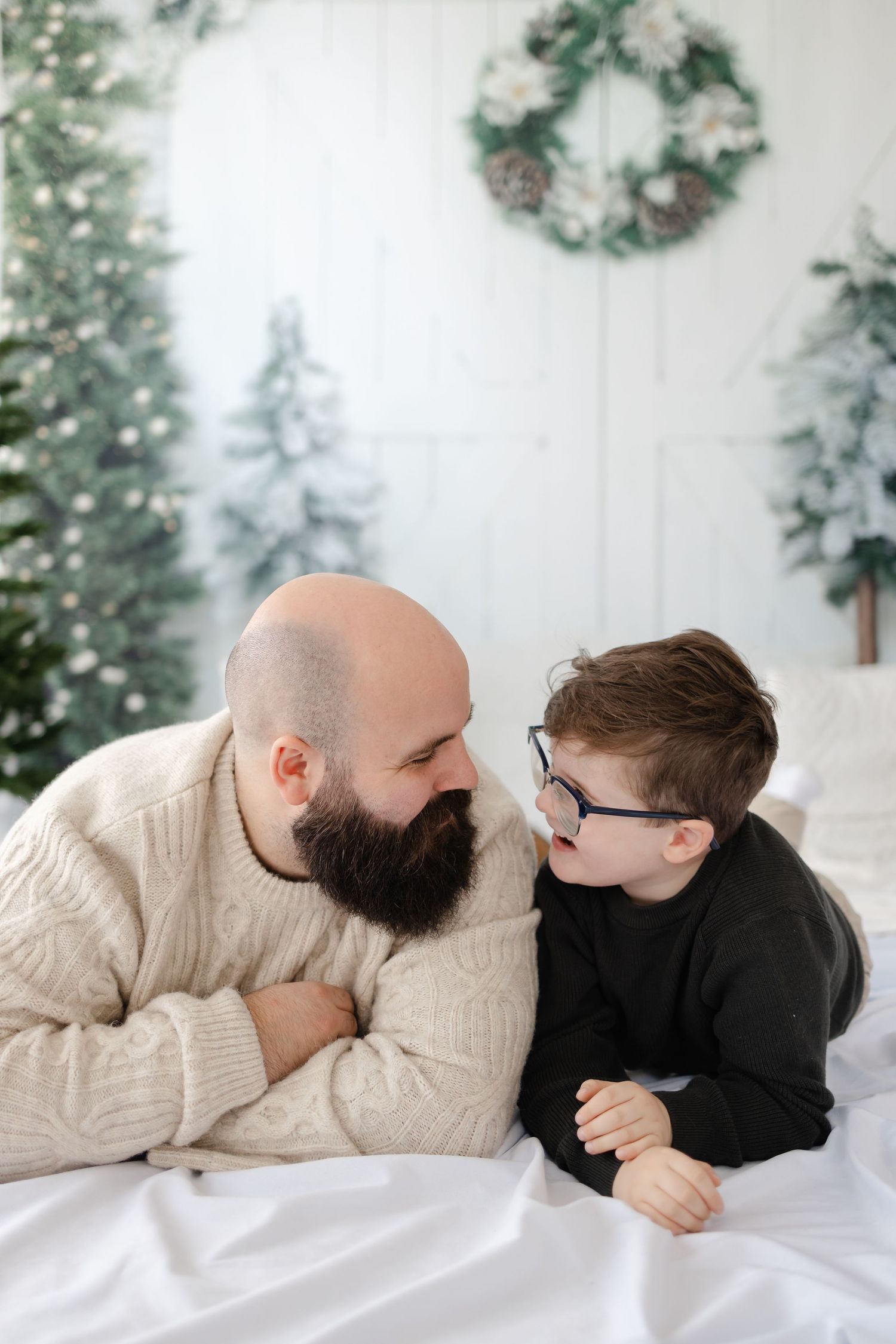Cozy winter portrait in front of Christmas trees and wreath on white background.