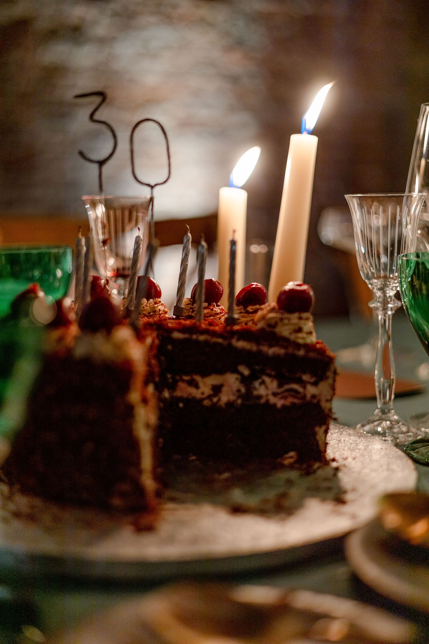 Close-up of chocolate birthday cake with lit candles in moody lighting.