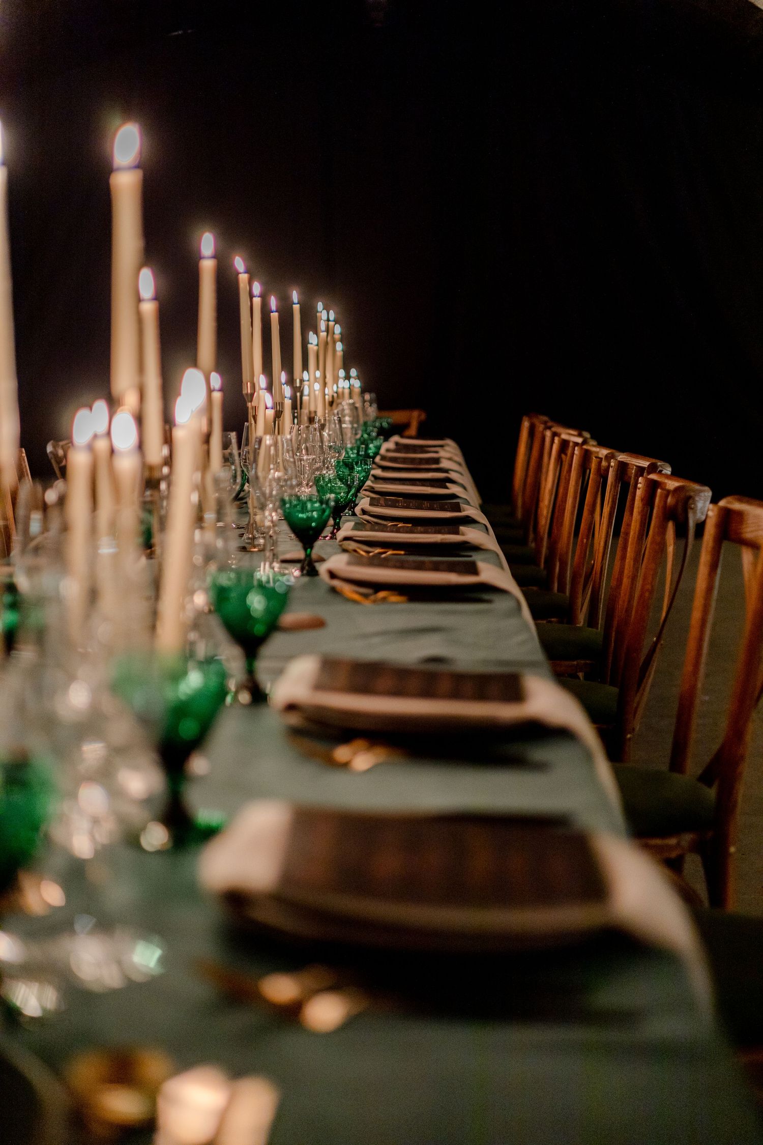 Candlelit dinner table with emerald green glasses and elegant place settings.
