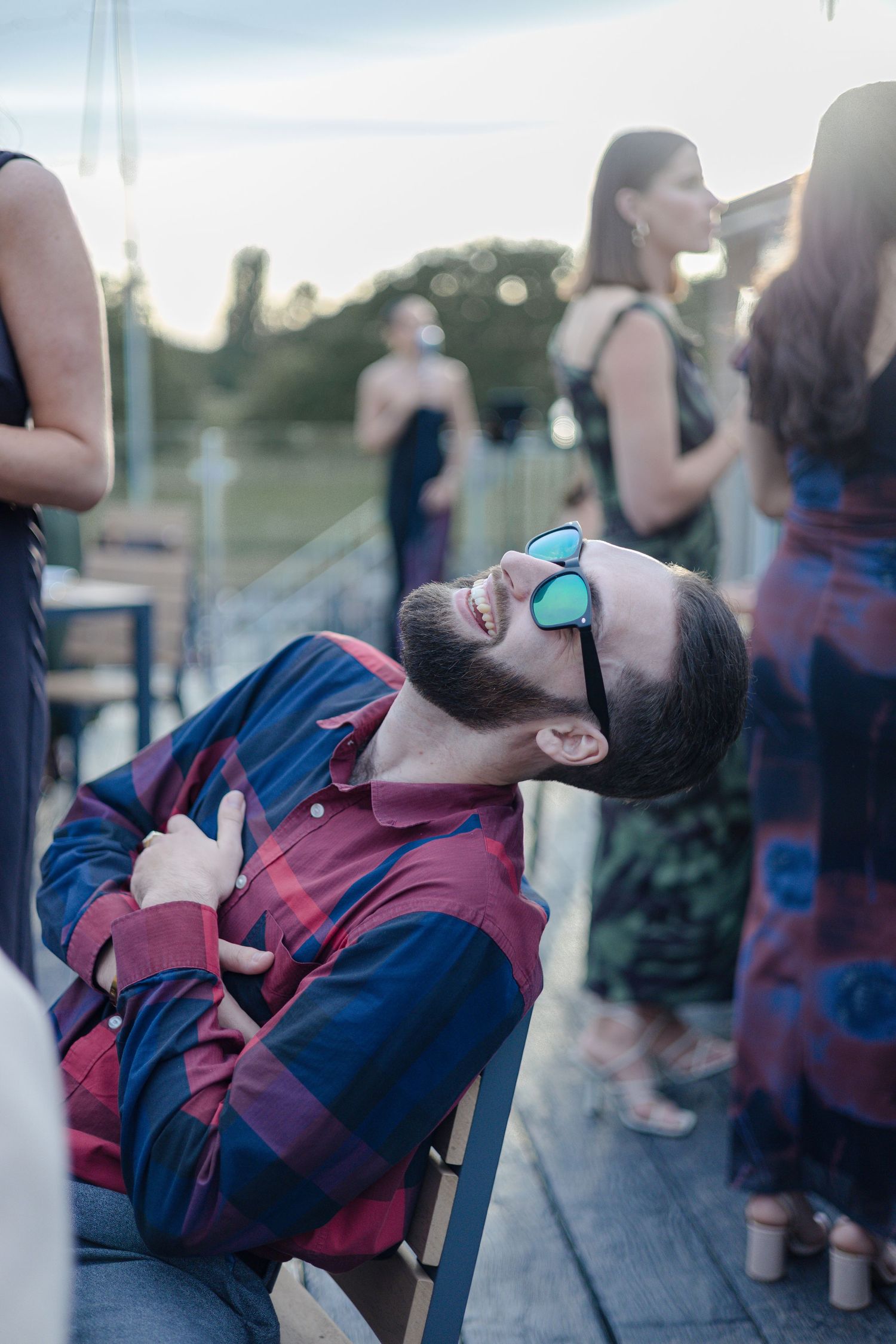 Person in sunglasses and striped jacket reclines in chair at outdoor gathering.