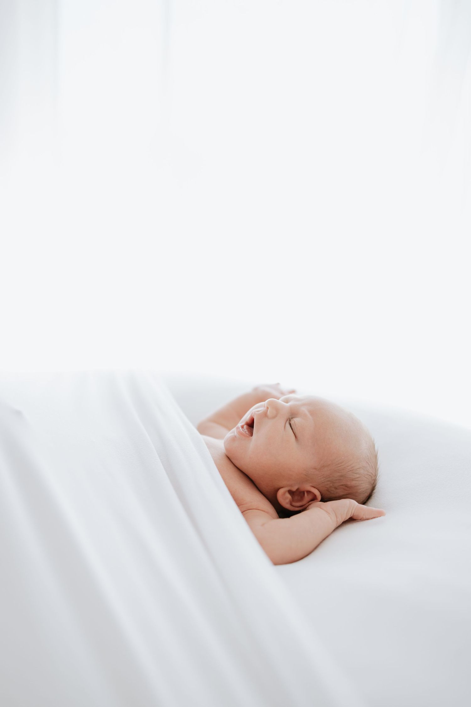 Peaceful sleeping newborn photographed in soft white bedding with minimalist style.