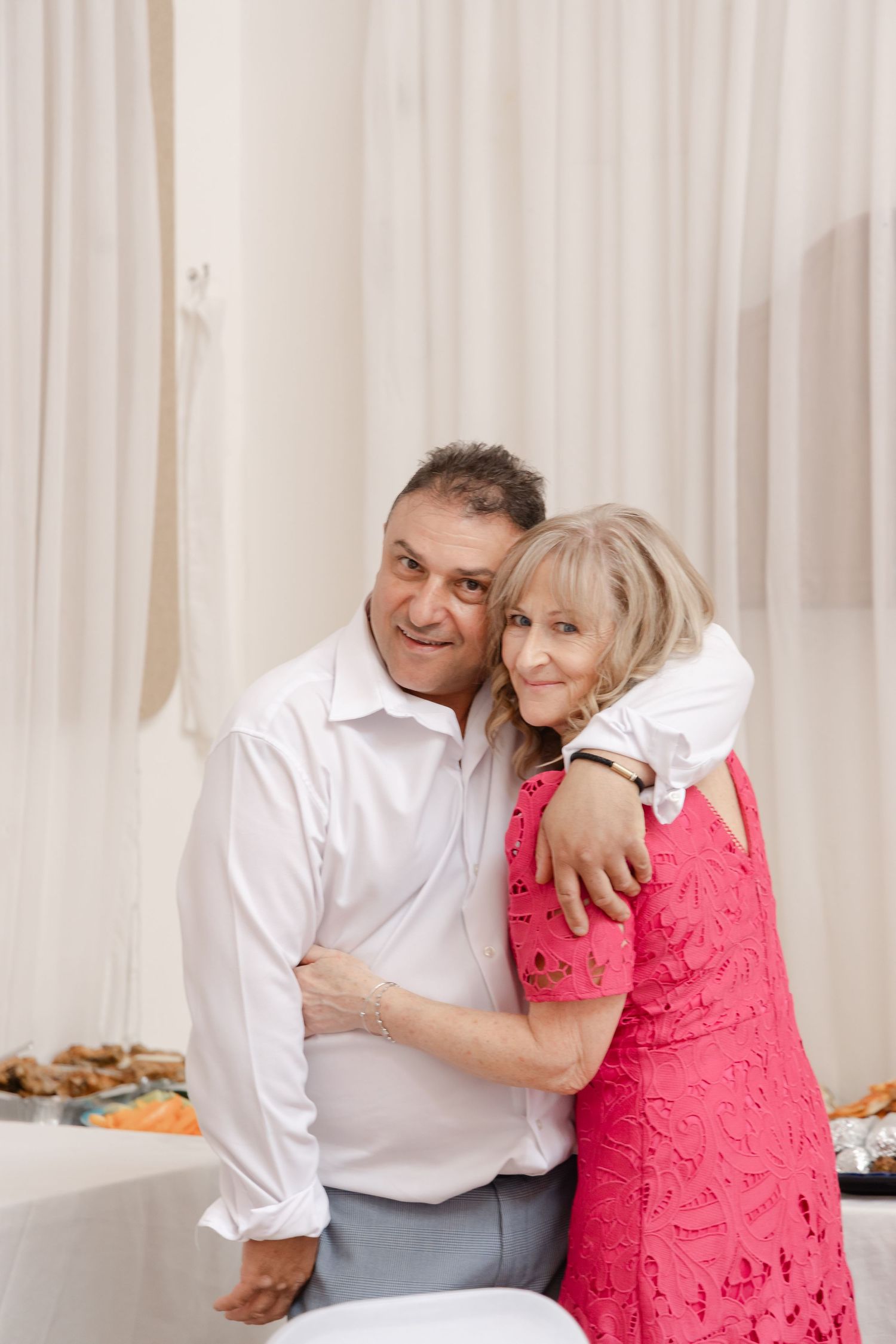 A couple shares an affectionate moment during a dance in a room with white curtains.