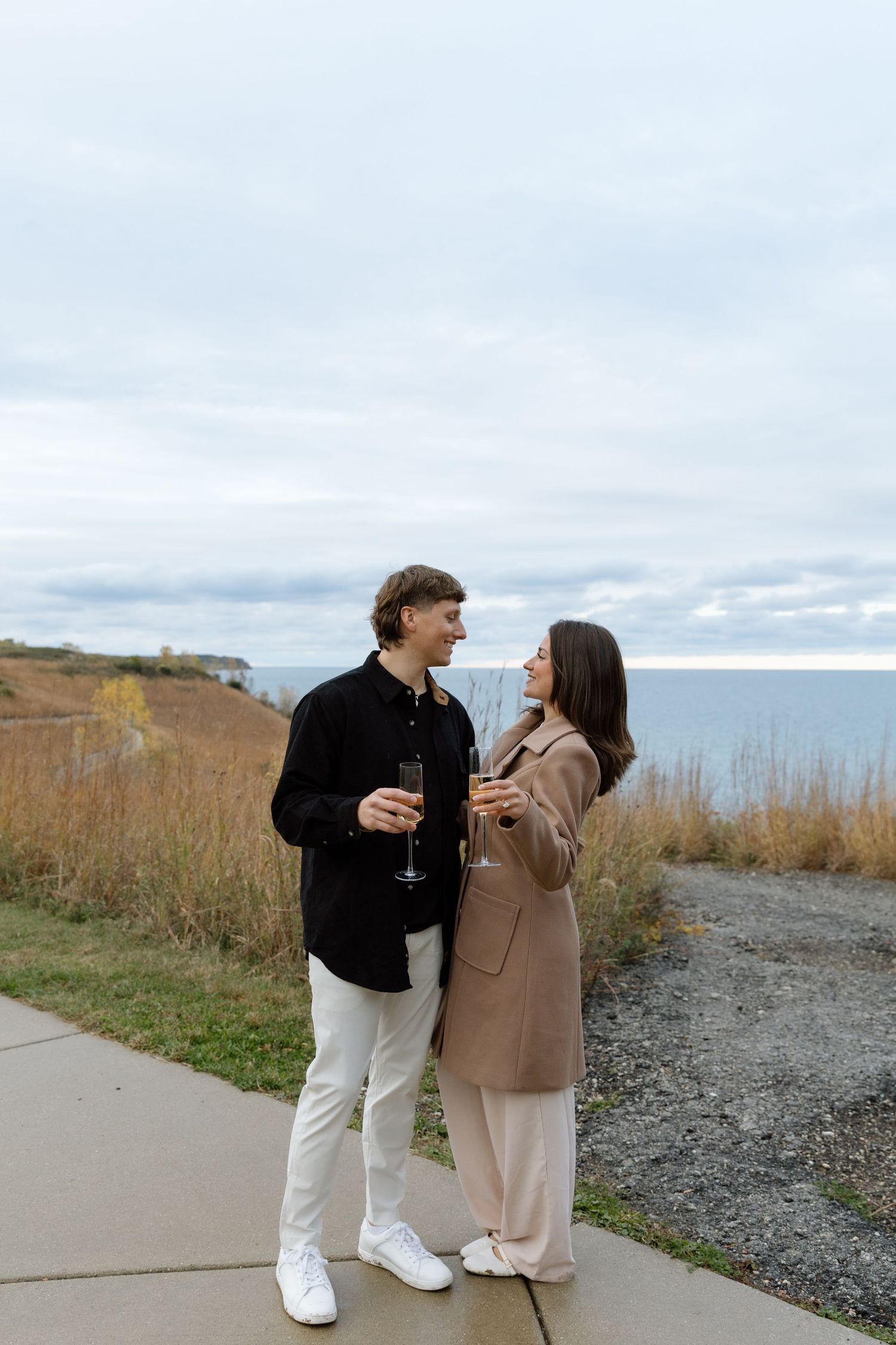 A couple shares champagne while walking along a coastal path.