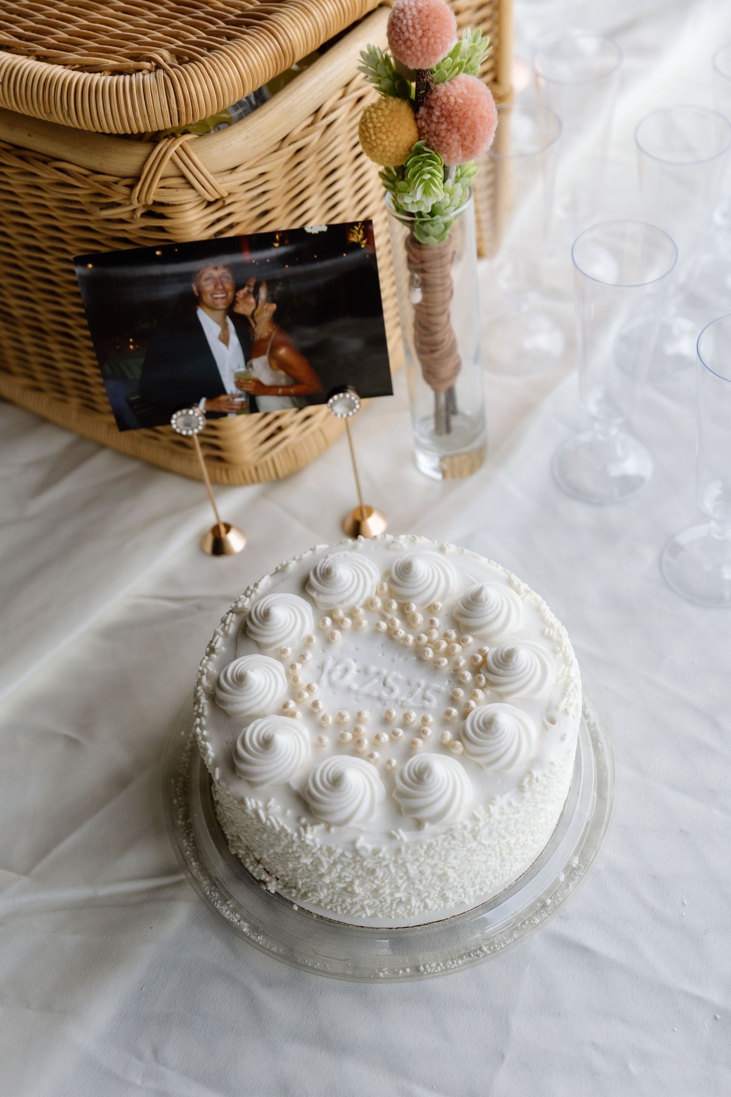 An elegant white wedding cake with pearl details and delicate frosting roses sits on a white tablecloth.