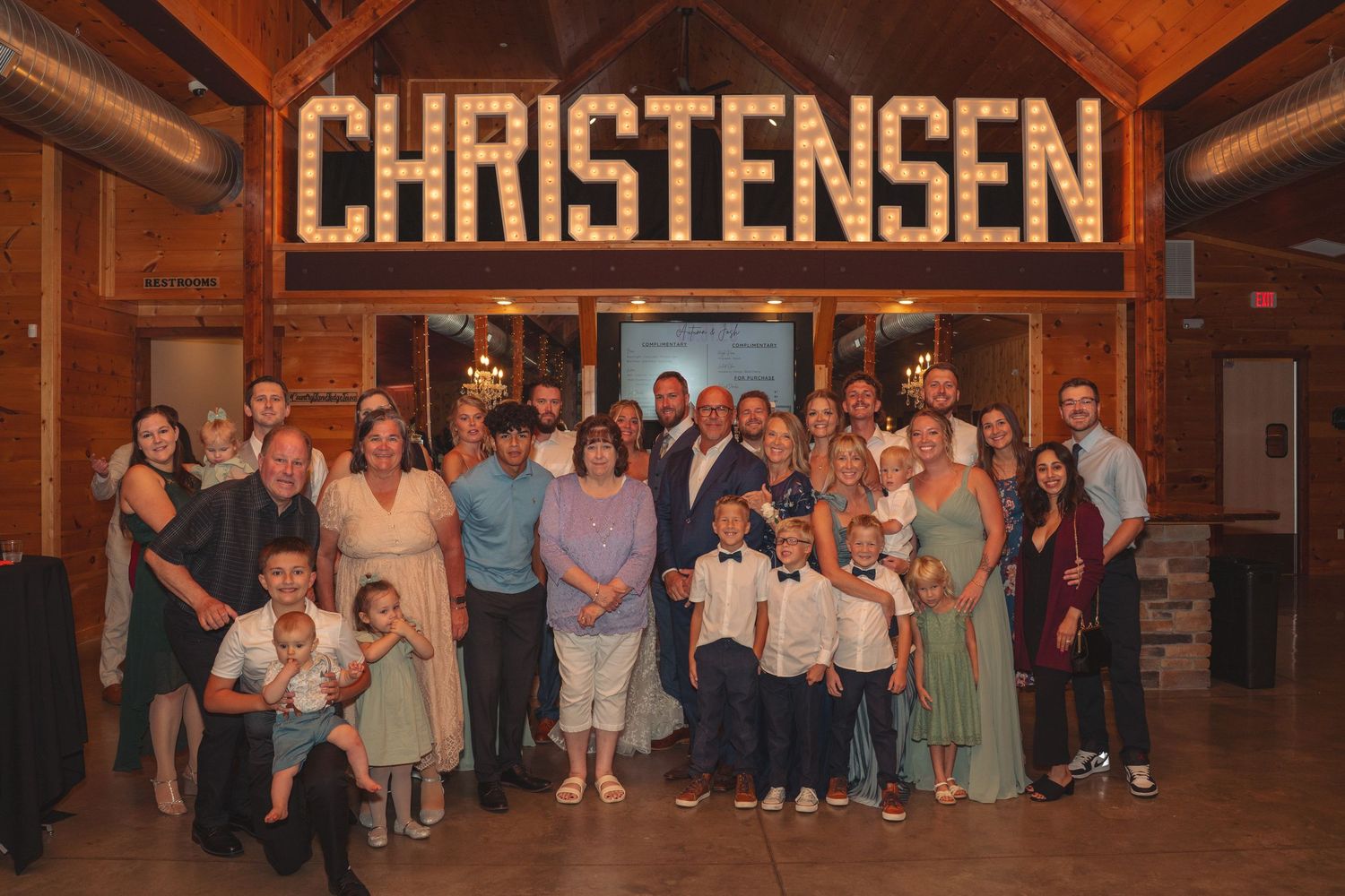 Large group of wedding guests gathered under rustic wooden beams with Christensen signage.