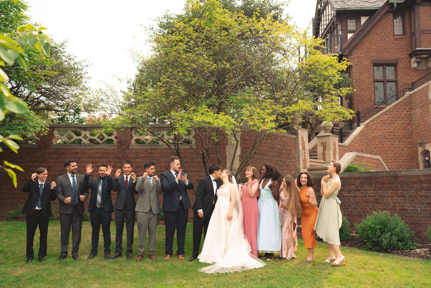 Wedding party members line up against brick building backdrop in formal attire.