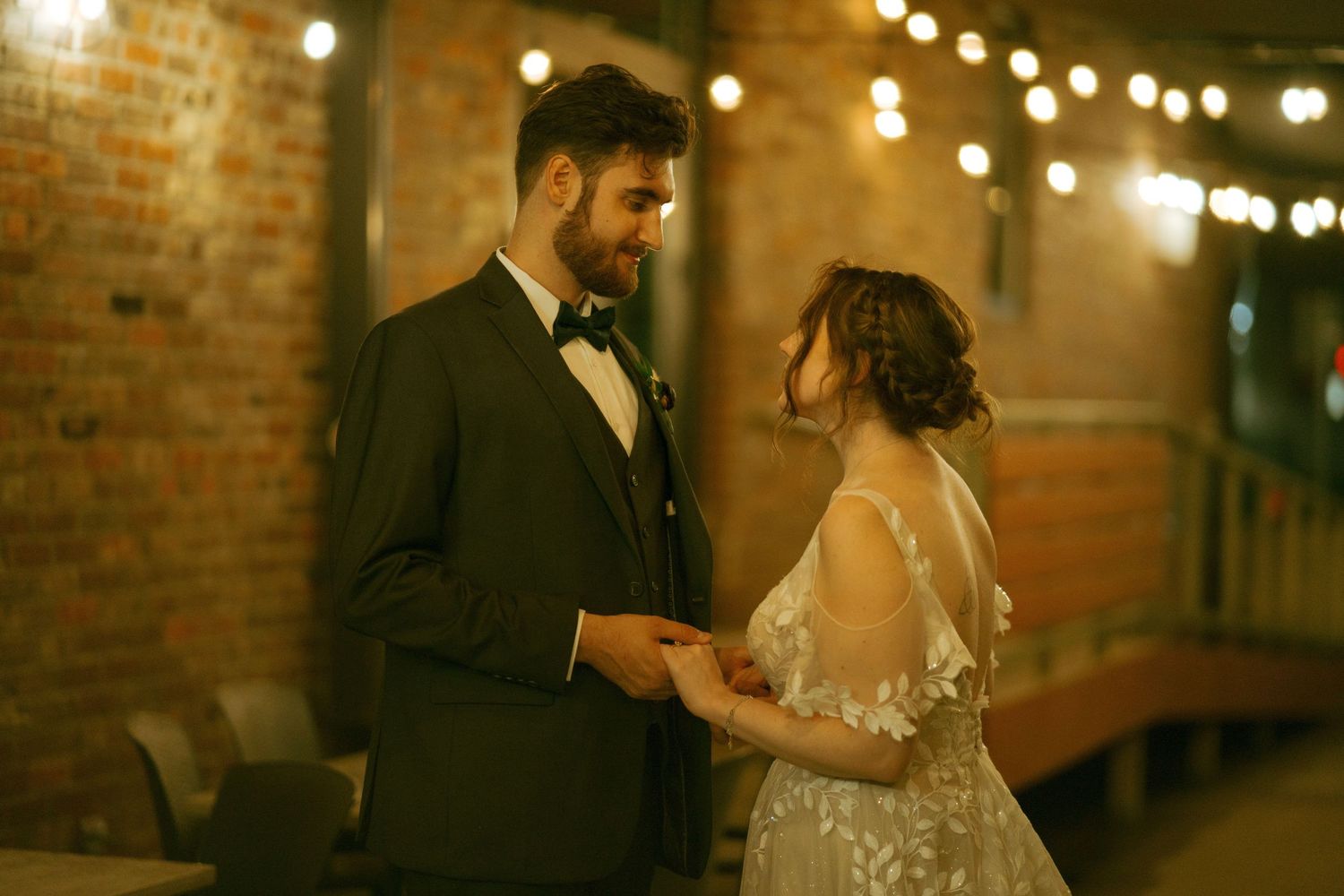 Couple sharing an intimate moment at their wedding reception with string lights and brick walls.