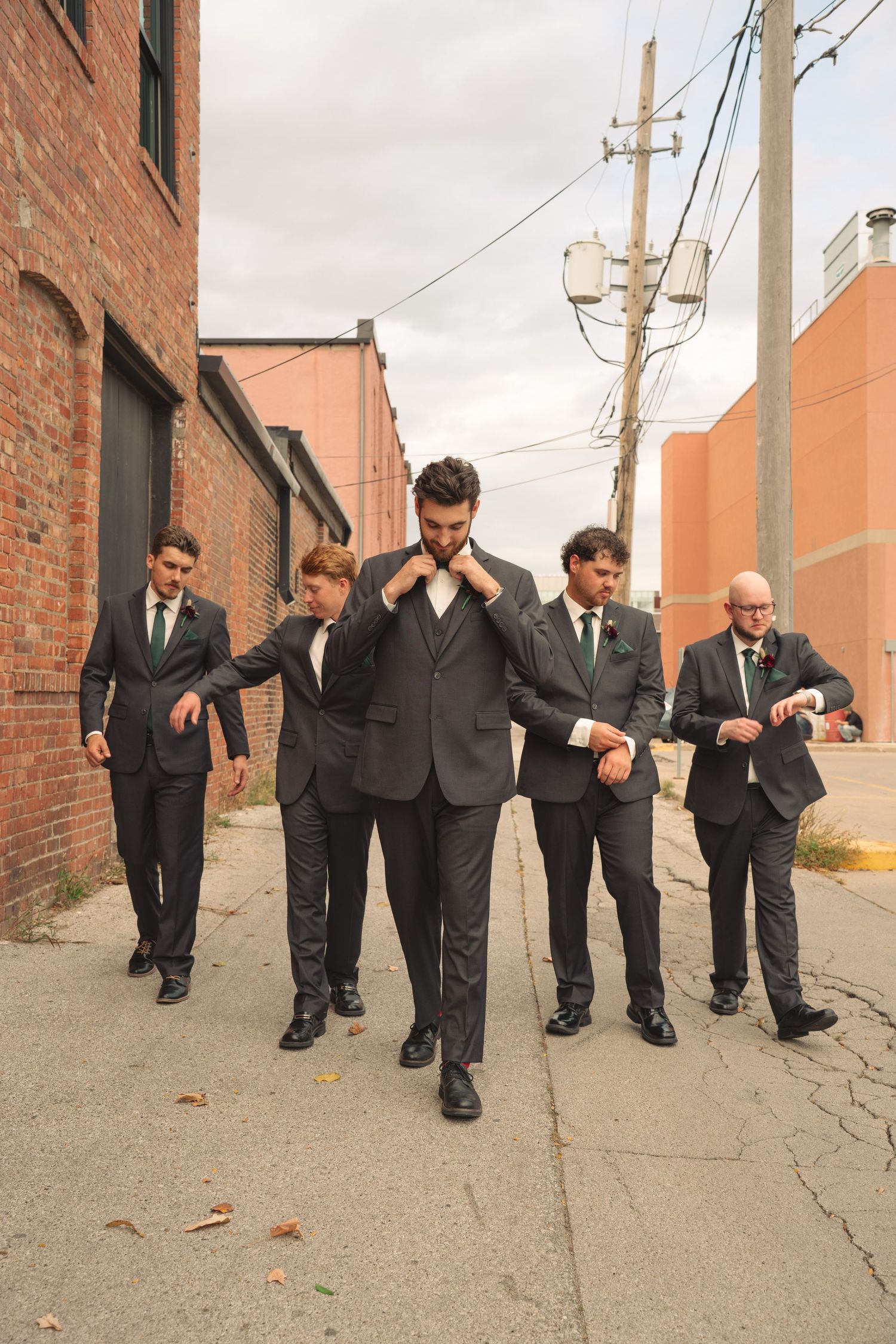 Groomsmen walk in formation down urban alley wearing matching dark suits.