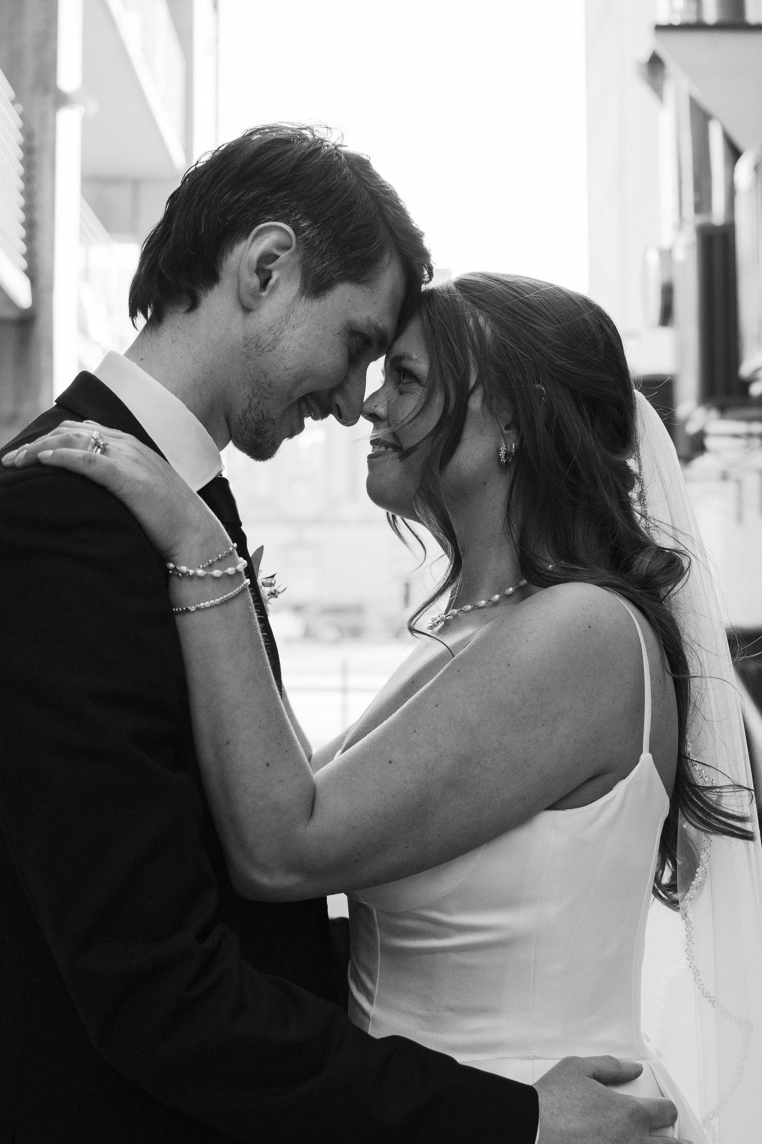 Romantic black and white close-up of bride and groom touching foreheads, smiling during wedding day.