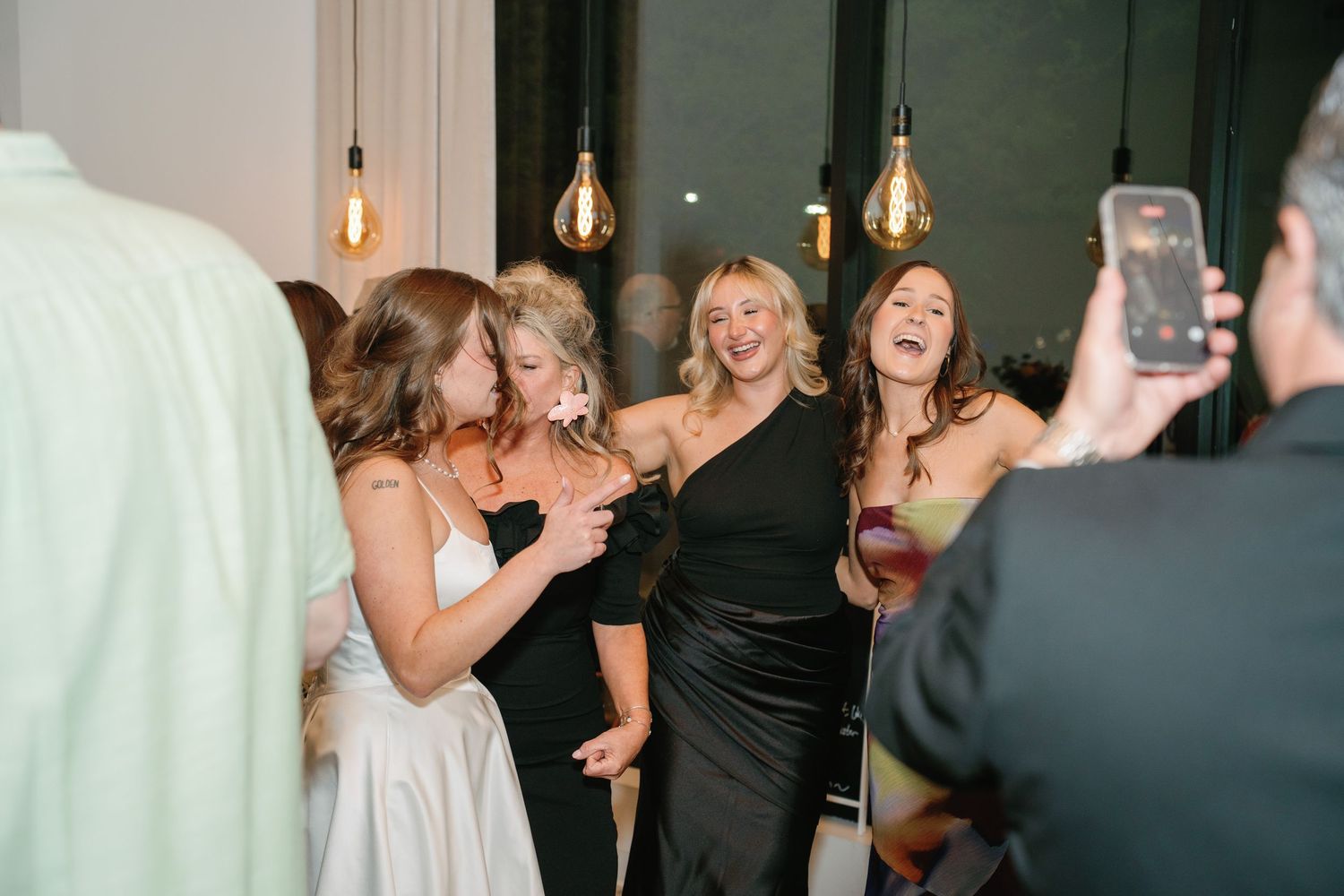 Women in elegant black and white dresses laughing and posing for a photo at a wedding reception.