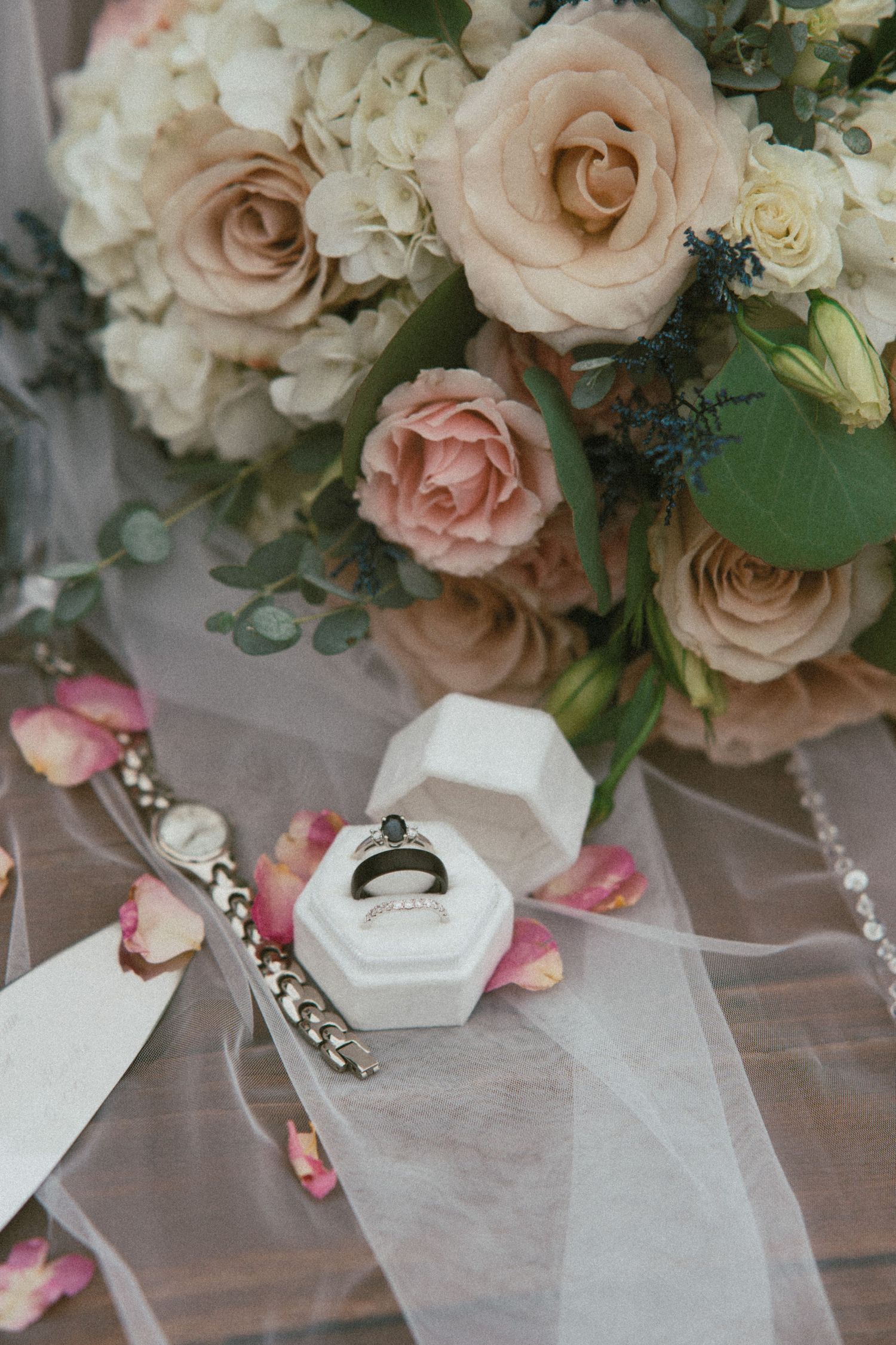 Elegant wedding details with pink roses and white floral arrangements on a wooden surface.