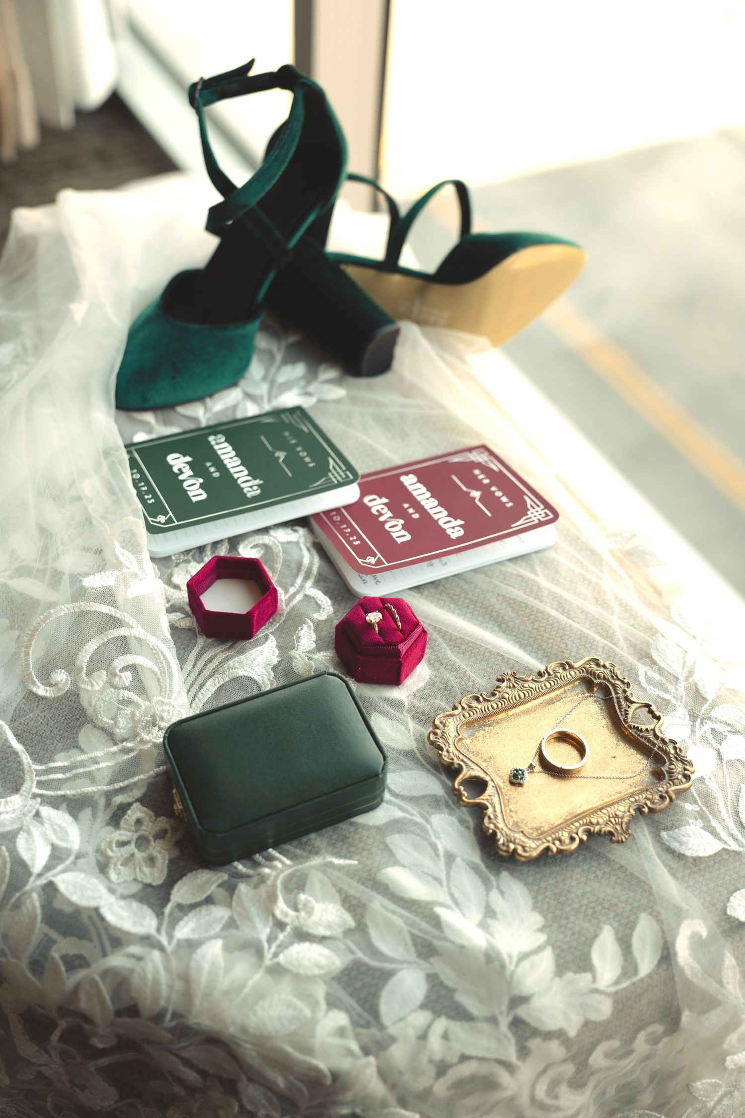 Wedding accessories including green velvet shoes, decorative cards and trinkets arranged on lace fabric.
