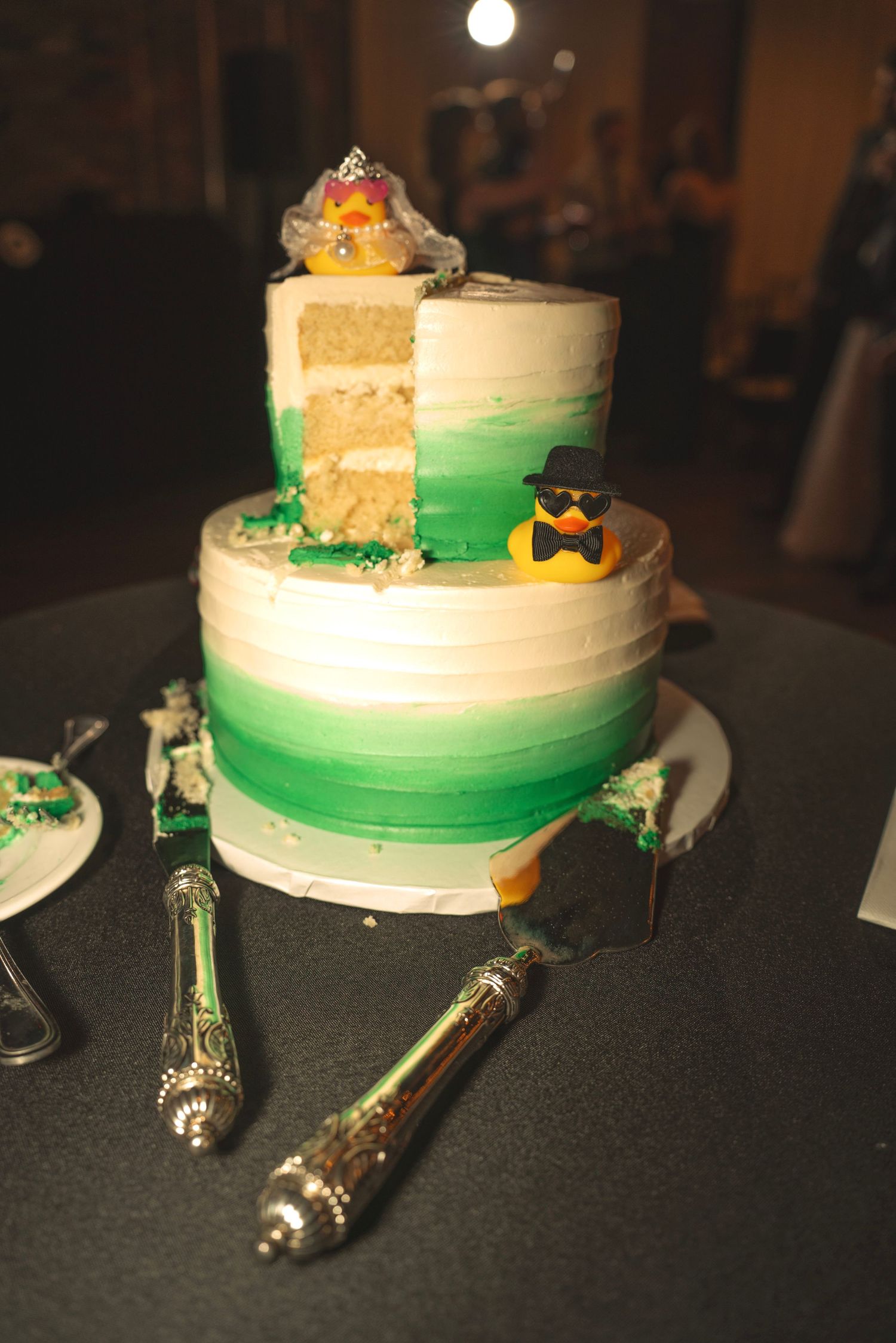 Wedding cake with green ombre design and decorative cake serving utensils on dark table.