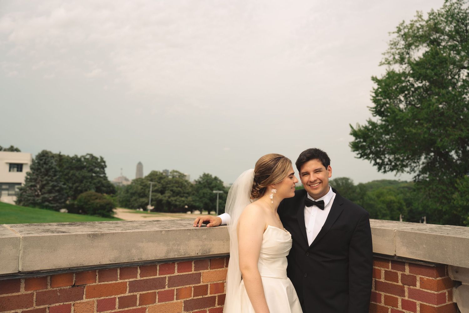 Wedding couple poses against brick wall backdrop in garden setting.
